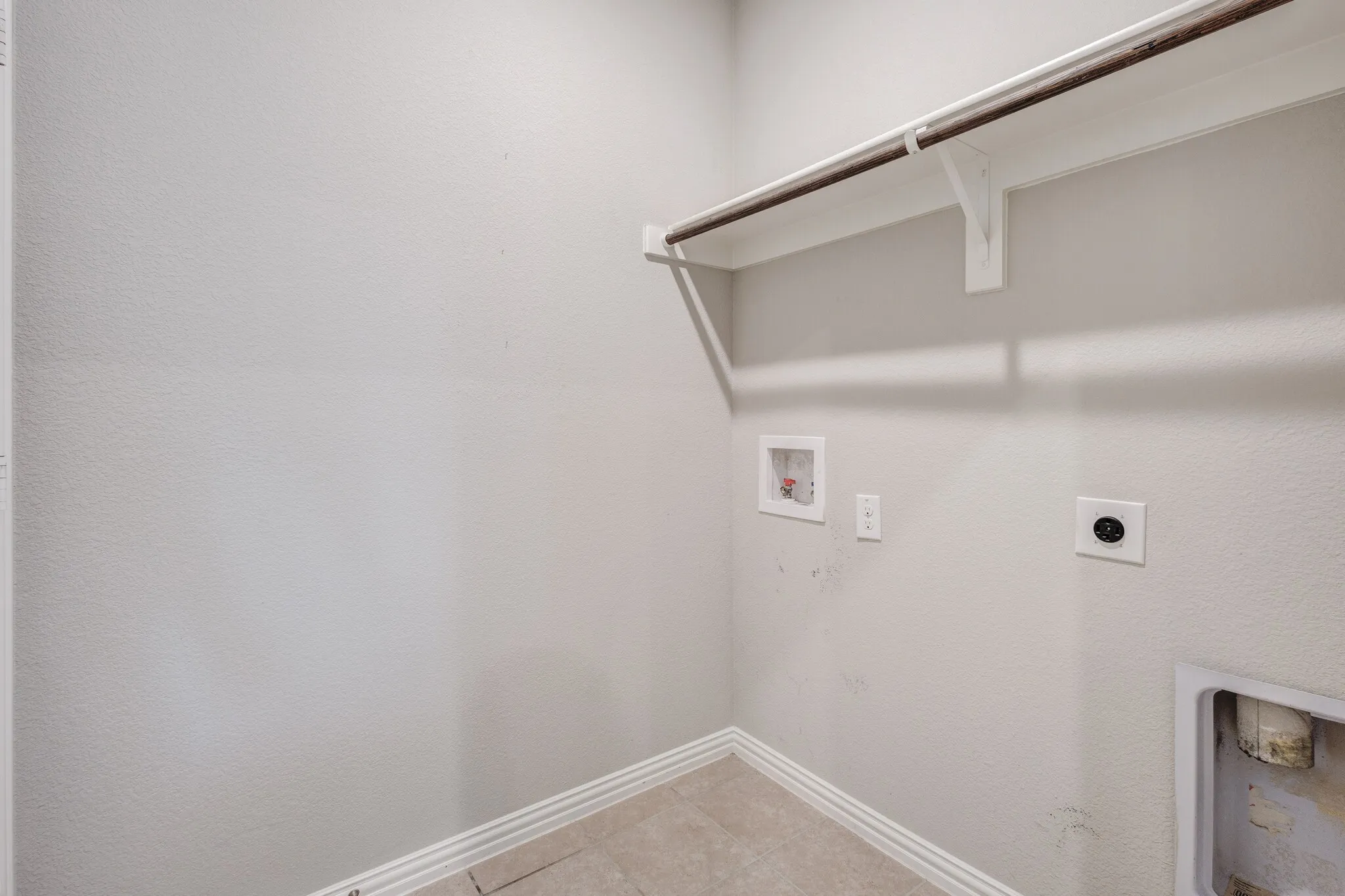 Neutral wall color, wall-mounted clothes rod, washer hookups, dryer hookups, and tiled flooring