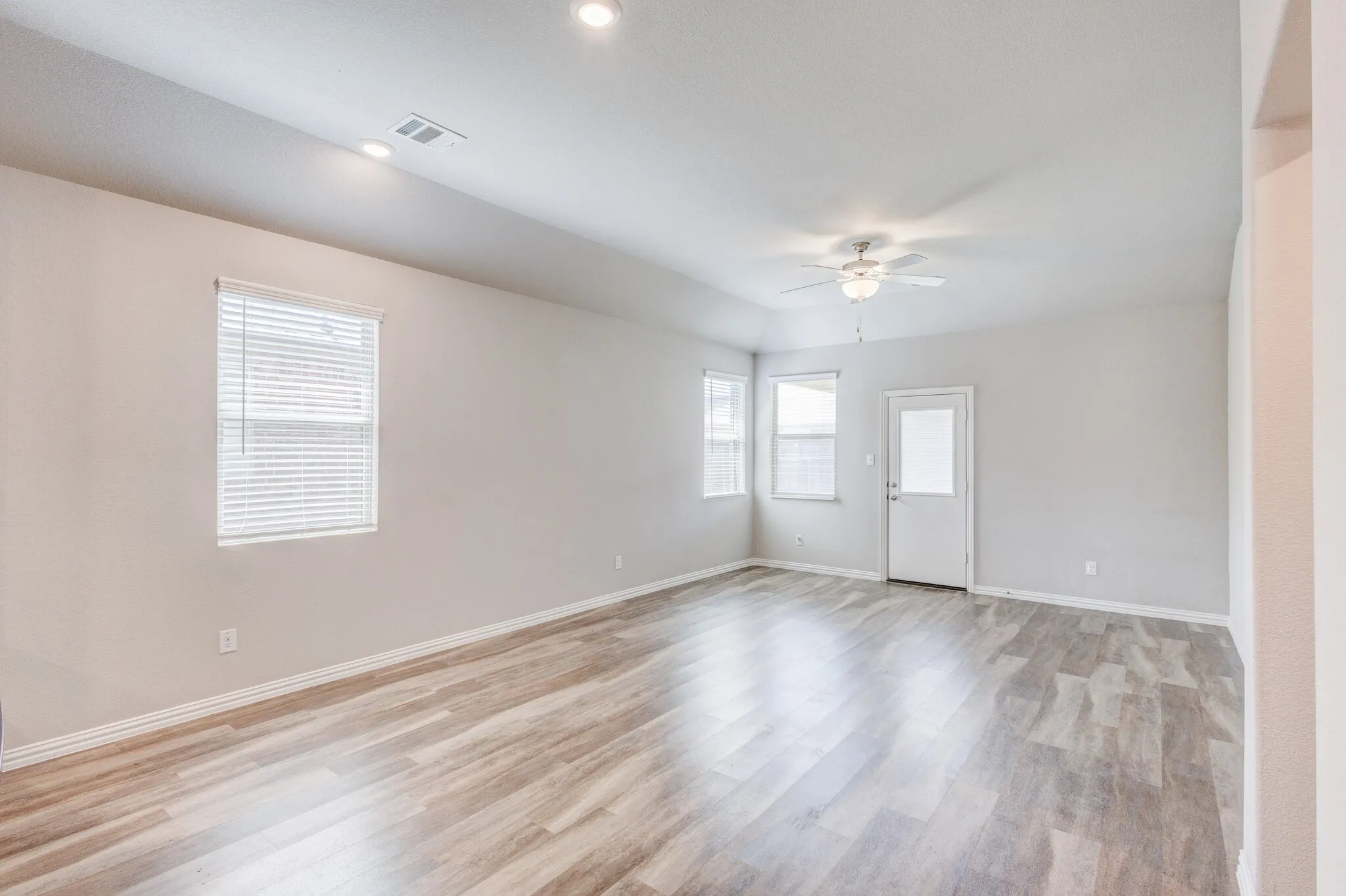 Spacious room featuring wood-finish flooring, multiple windows with blinds, a ceiling fan, and recessed lighting
