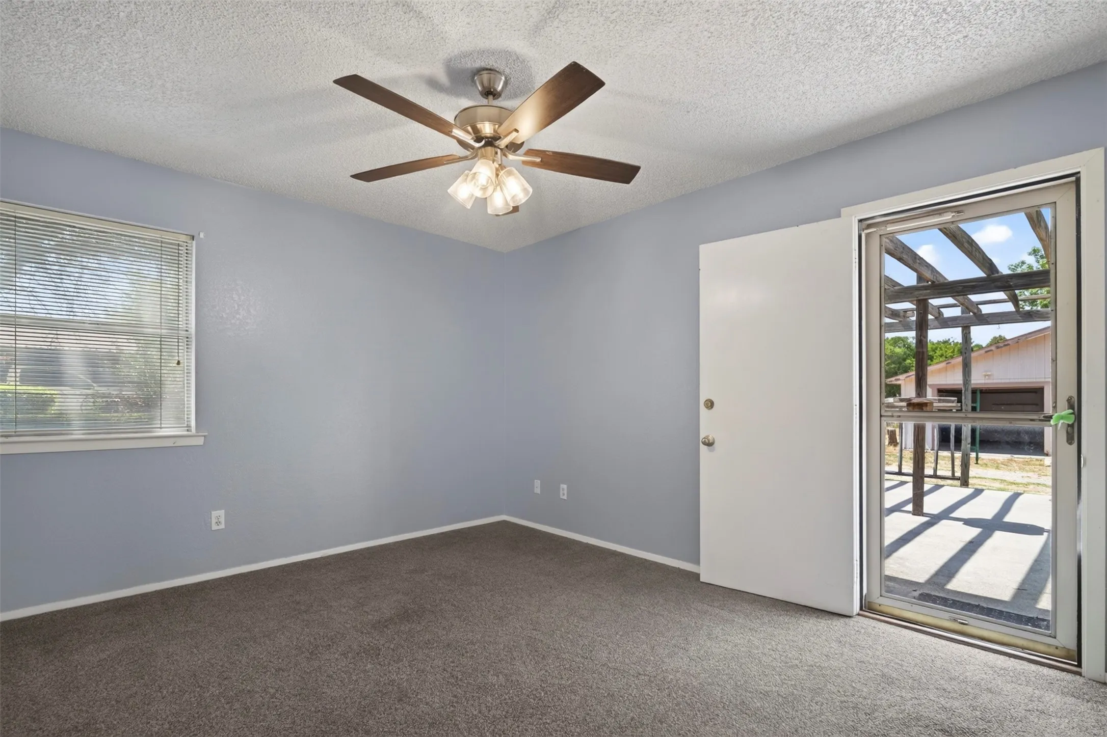 Textured wall finish, ceiling fan with integrated lighting, window with blinds, and exterior access door with screen