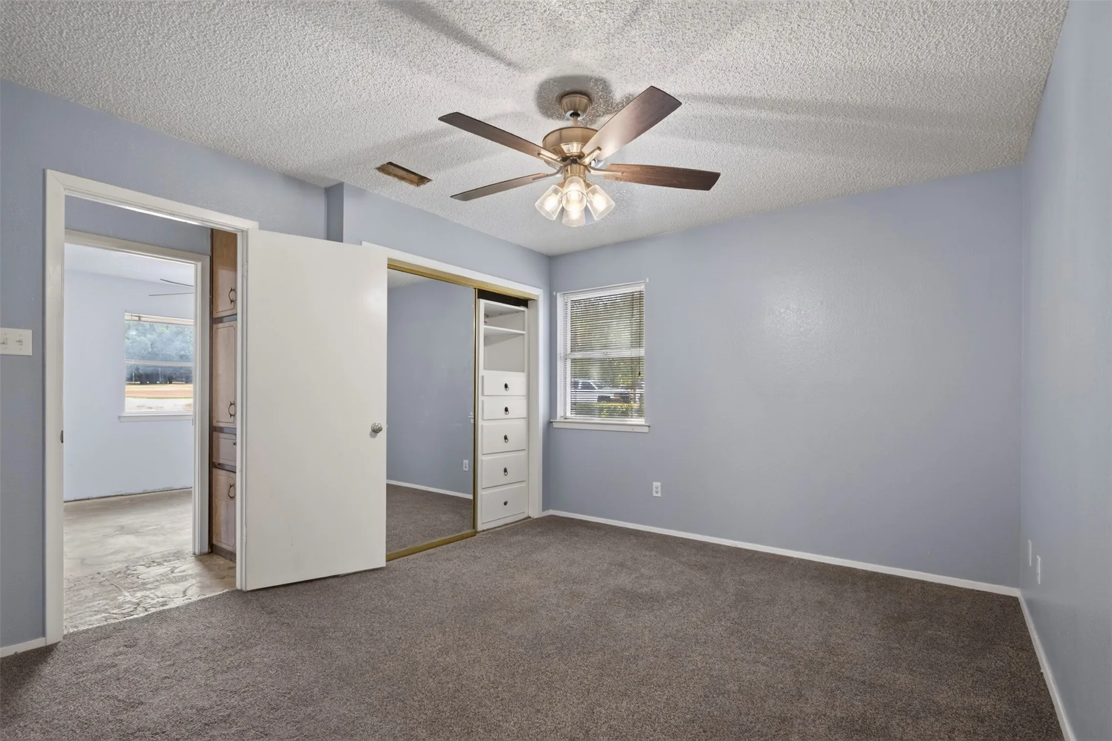 Carpeted flooring, ceiling fan with integrated lighting, window with exterior views, sliding mirrored closet doors, and built-in closet storage