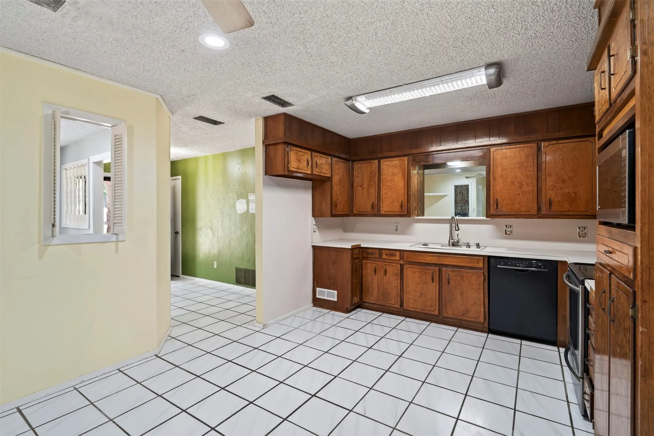 Kitchen featuring wood cabinetry, white countertops, stainless steel sink with faucet, built-in microwave, and tile flooring