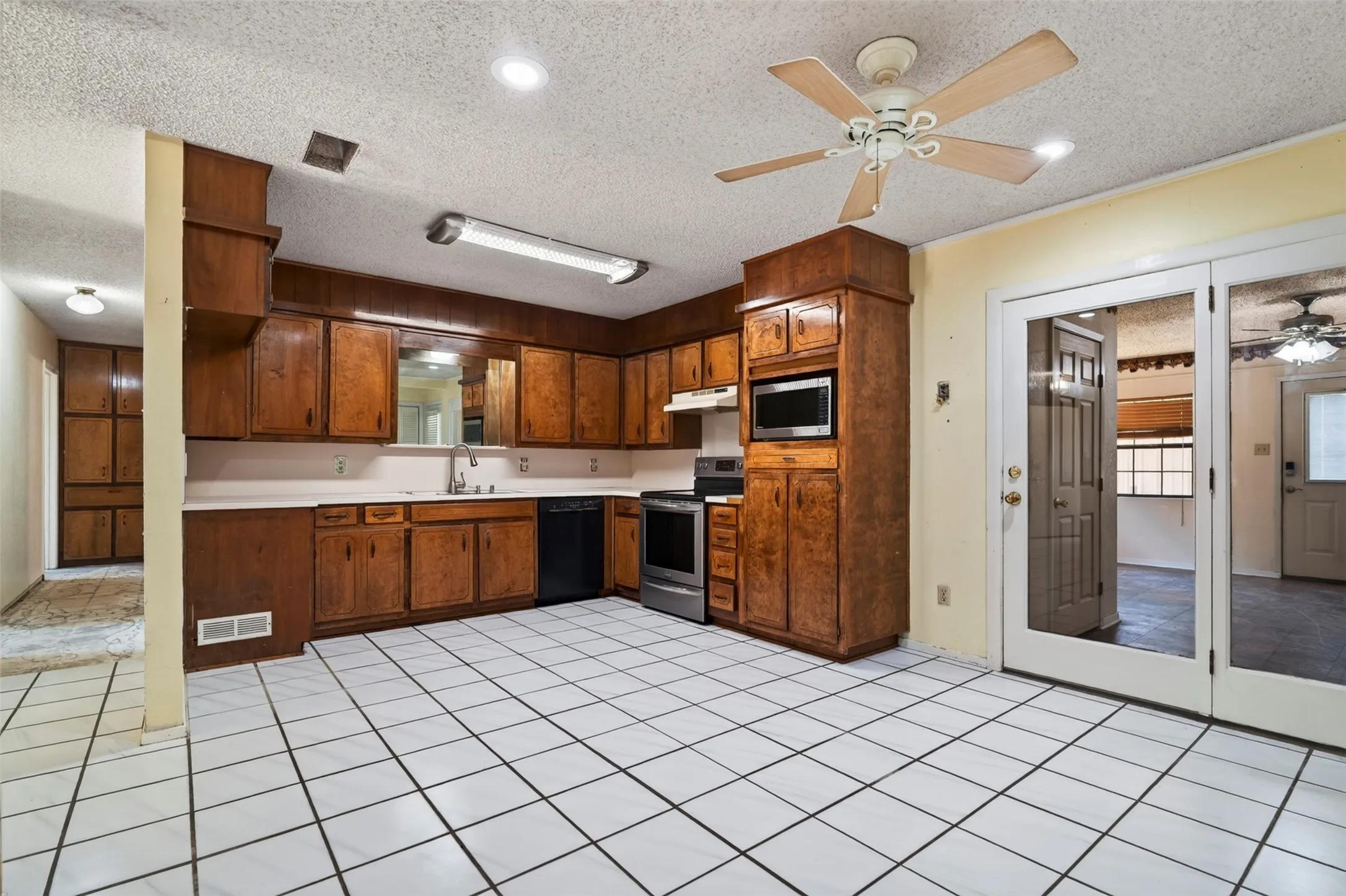 Kitchen featuring white tile flooring, wood cabinetry, built-in microwave, stainless steel range, and a ceiling fan