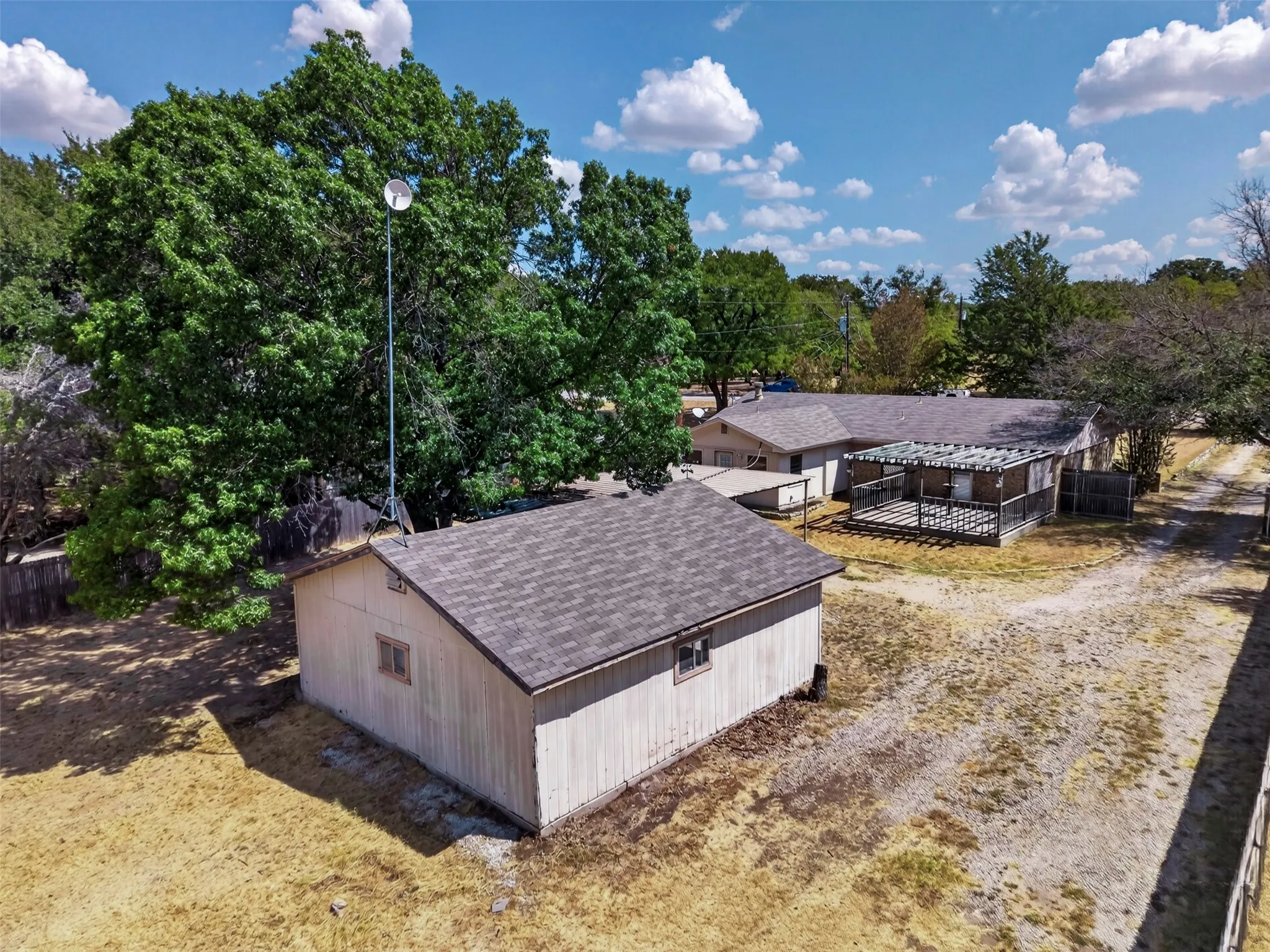 Detached storage building with a shingled roof, gravel pathway, and an expansive outdoor deck featuring a pergola