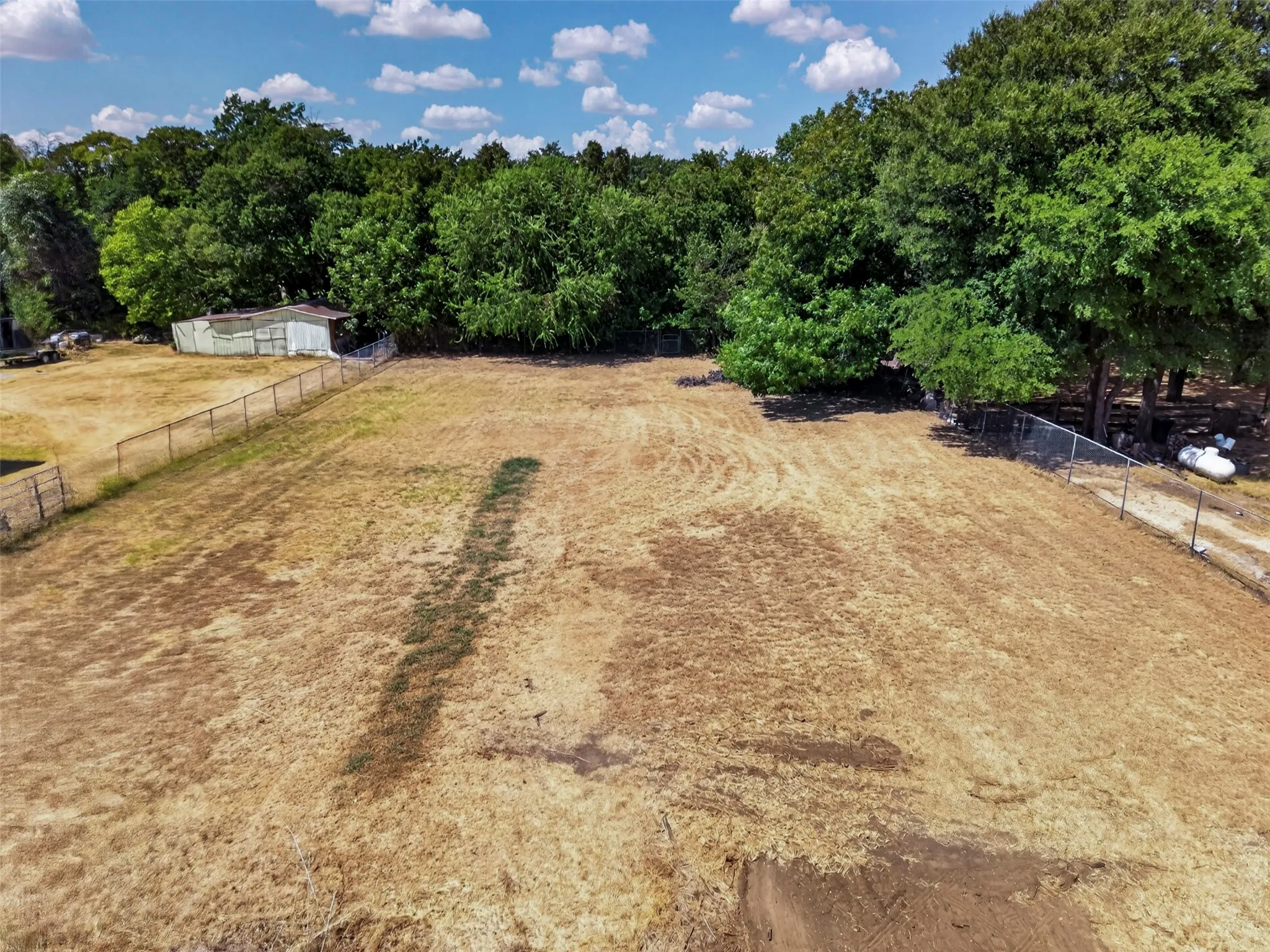 Expansive lot featuring a fenced perimeter, mature tree line, and visible outbuilding