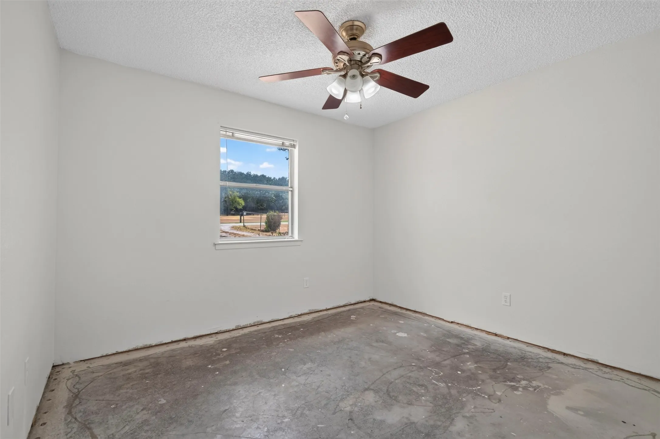 Single-pane window, ceiling-mounted light fixture with ceiling fan, textured ceiling, and concrete flooring
