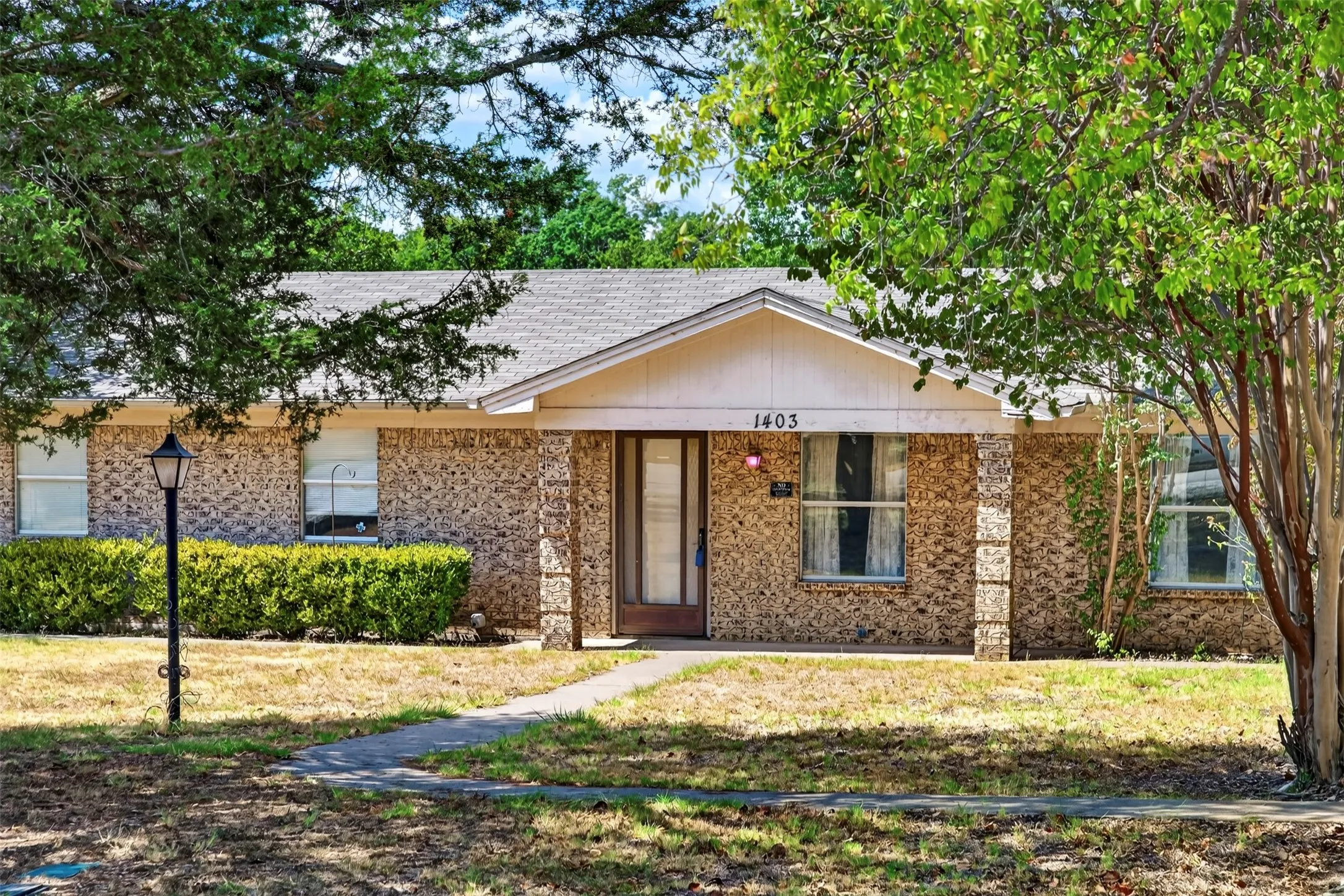 Brick exterior with a gabled roofline, covered porch, and mature trees