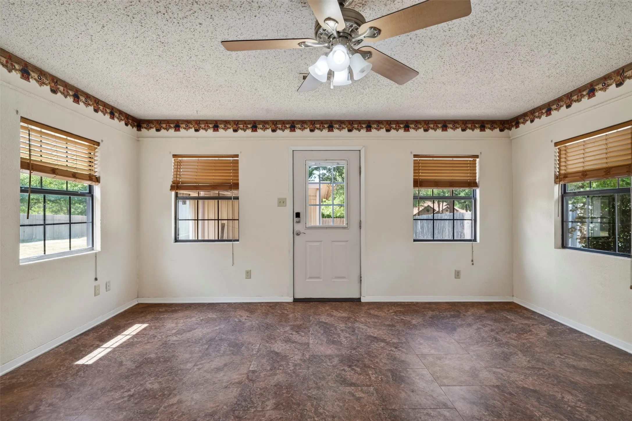 Wood-finish flooring, multiple windows with blinds, a glass-paned door, and a ceiling fan with integrated lighting