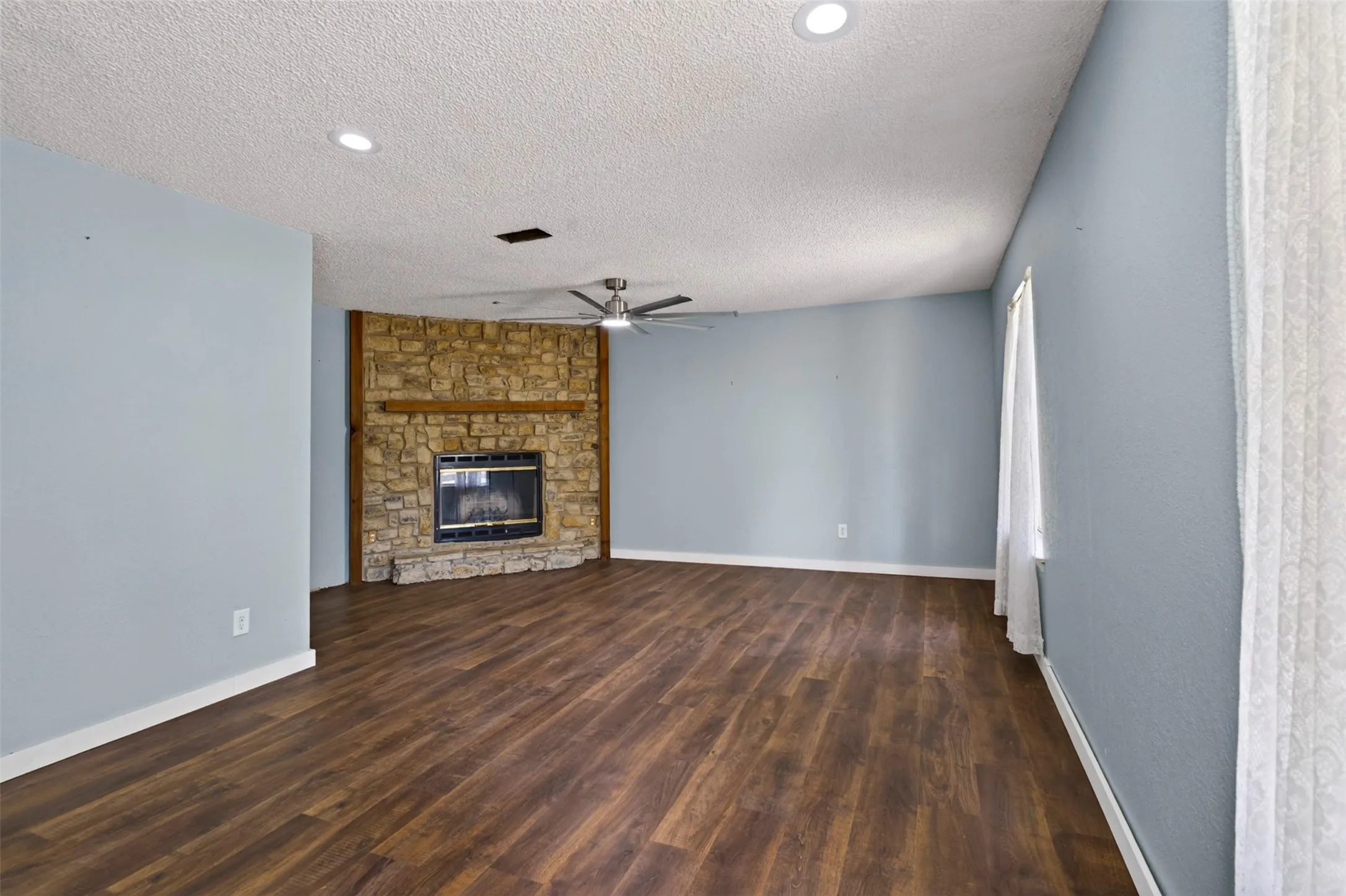 Stone-faced fireplace with a wood mantle, recessed lighting, ceiling fan, and wood-finish flooring