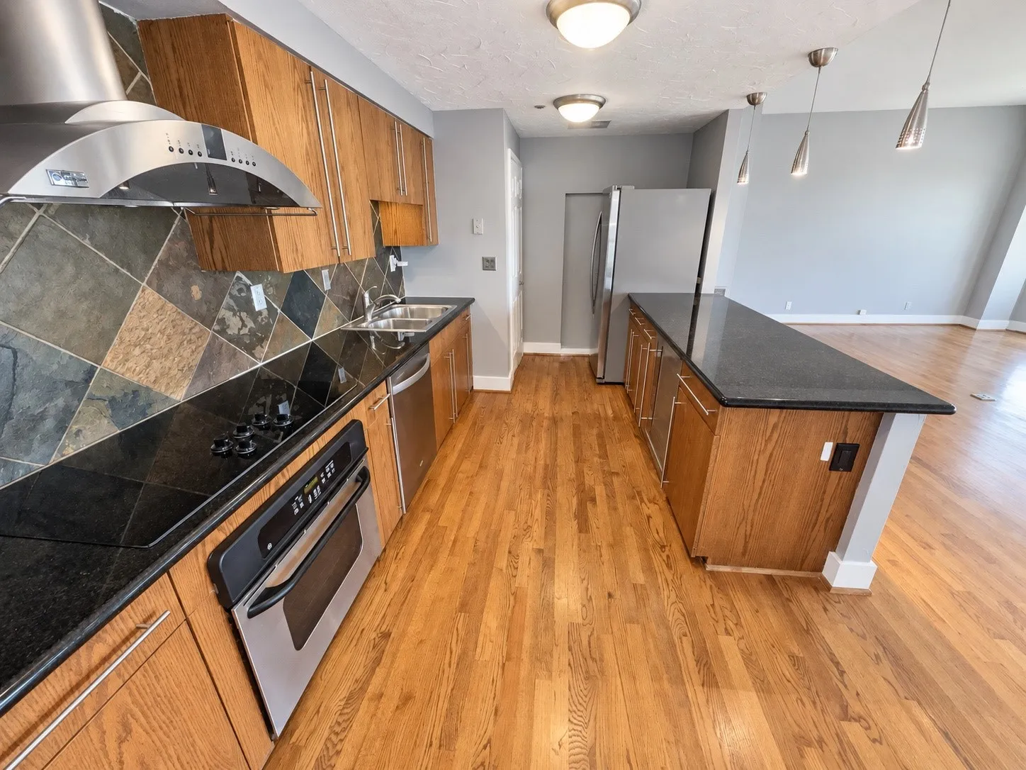 Kitchen featuring wood-finish cabinetry, black countertops, stainless steel appliances, and a diagonal tile backsplash