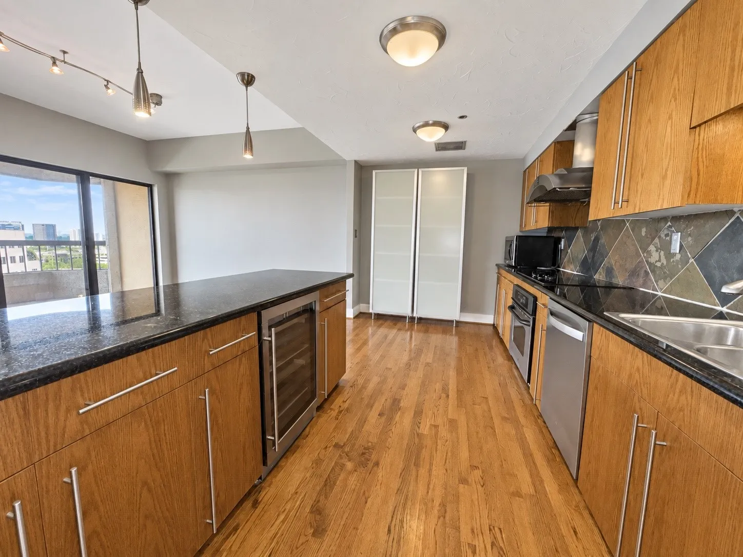 Hardwood flooring throughout, featuring a kitchen with granite countertops, stainless steel appliances, wood cabinetry, and a beverage refrigerator