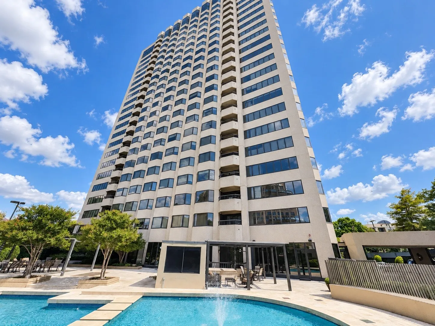 High-rise building with a tiered facade, individual balconies, and a ground-level swimming pool with water feature