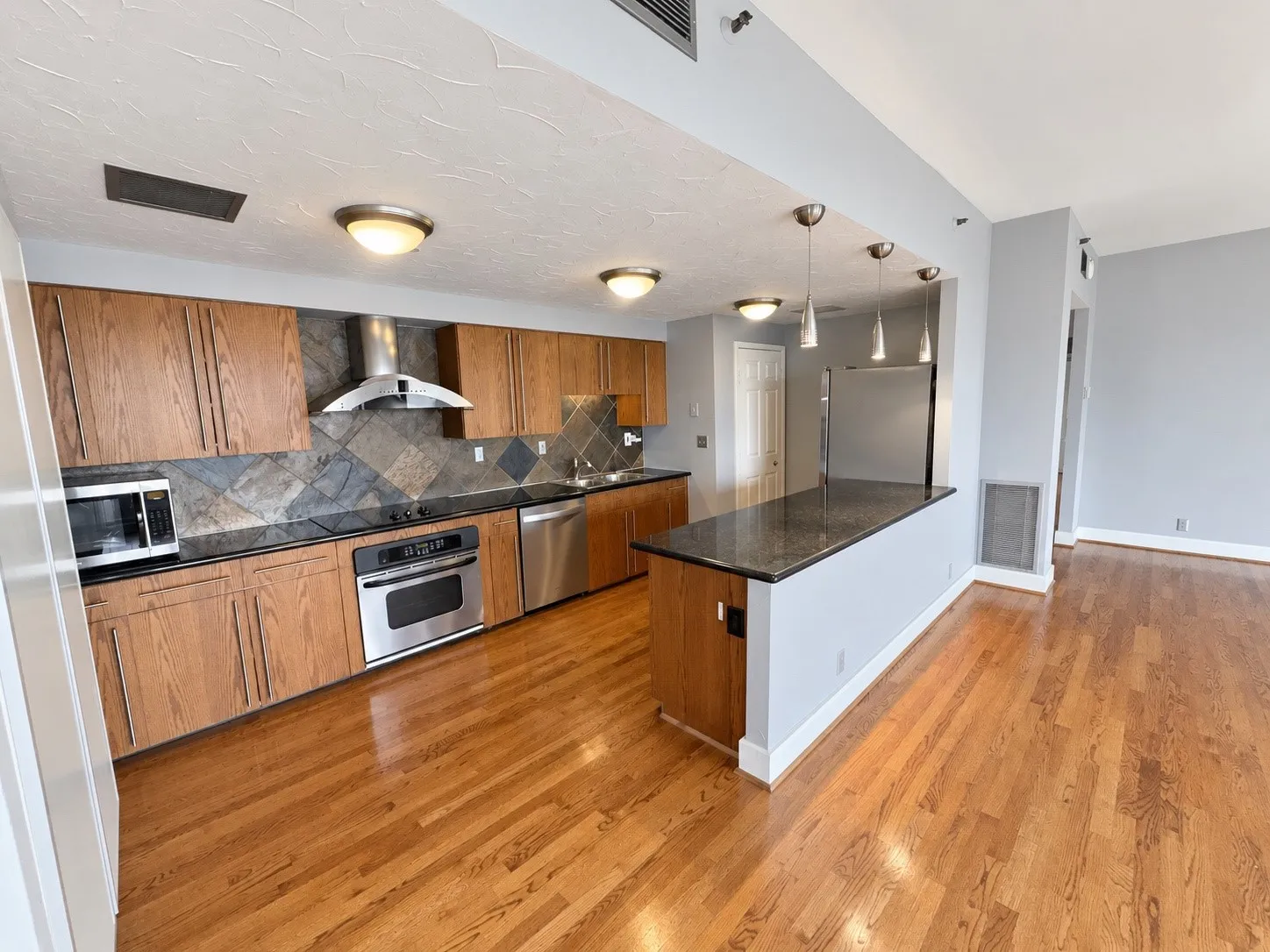 Hardwood flooring, stainless steel appliances, dark stone countertops, kitchen island, and wood cabinetry