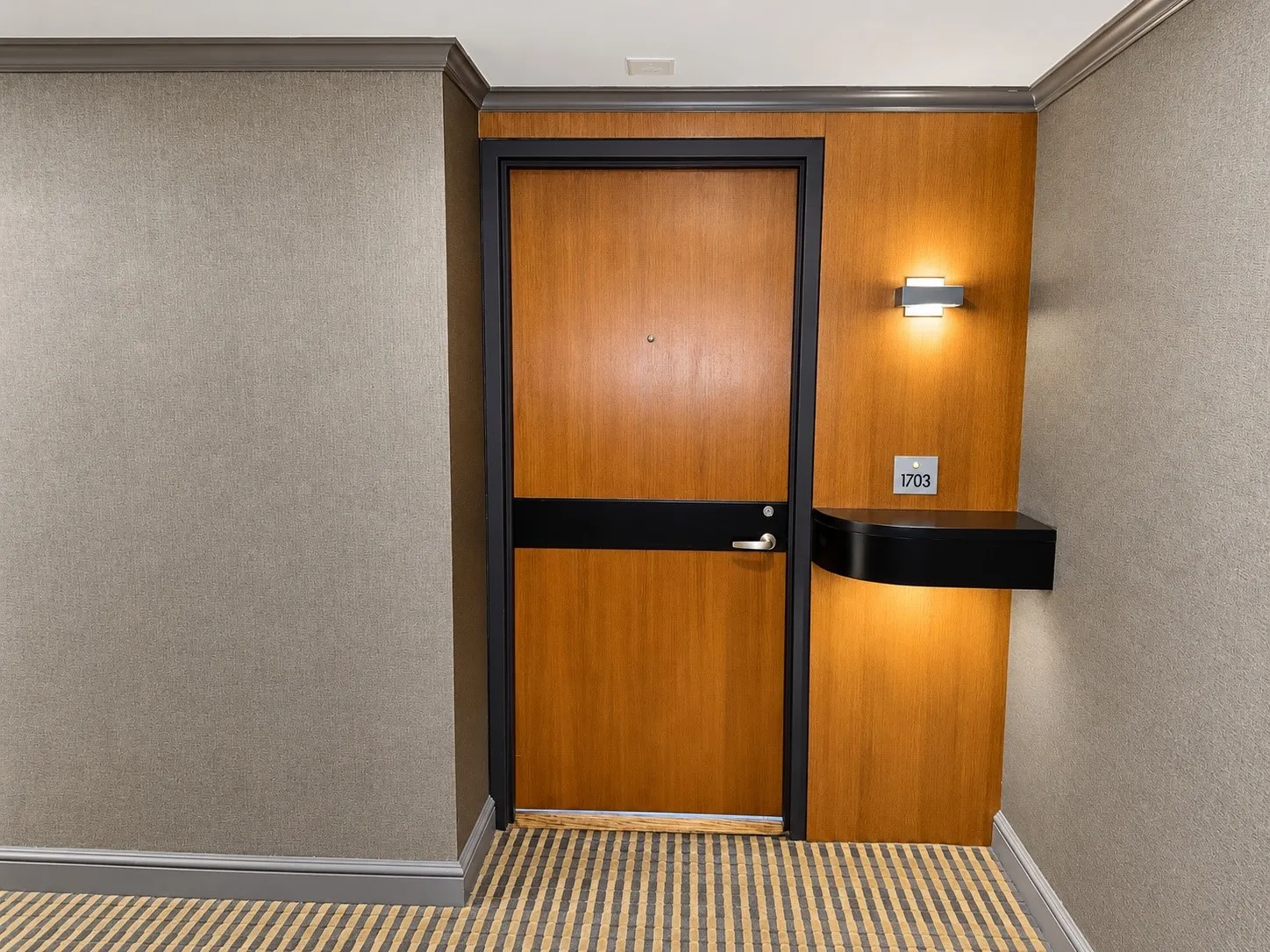Wood-finish entry door with dark trim, textured wall covering, and a patterned carpet