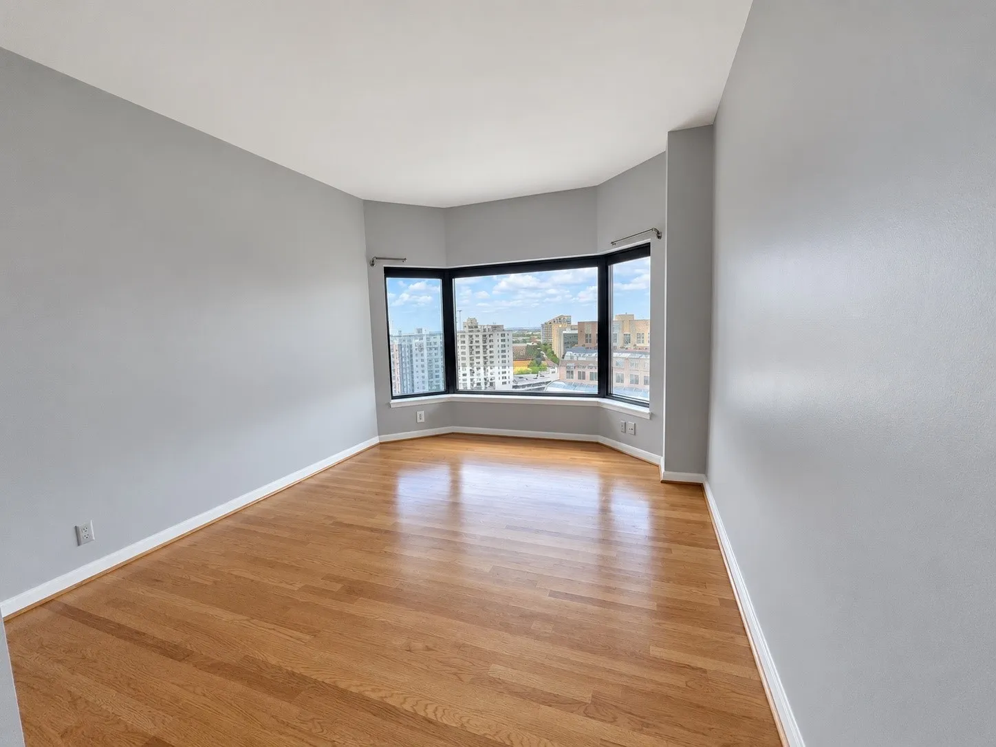 Bay window with city backdrop, wood-finish flooring, and light gray walls
