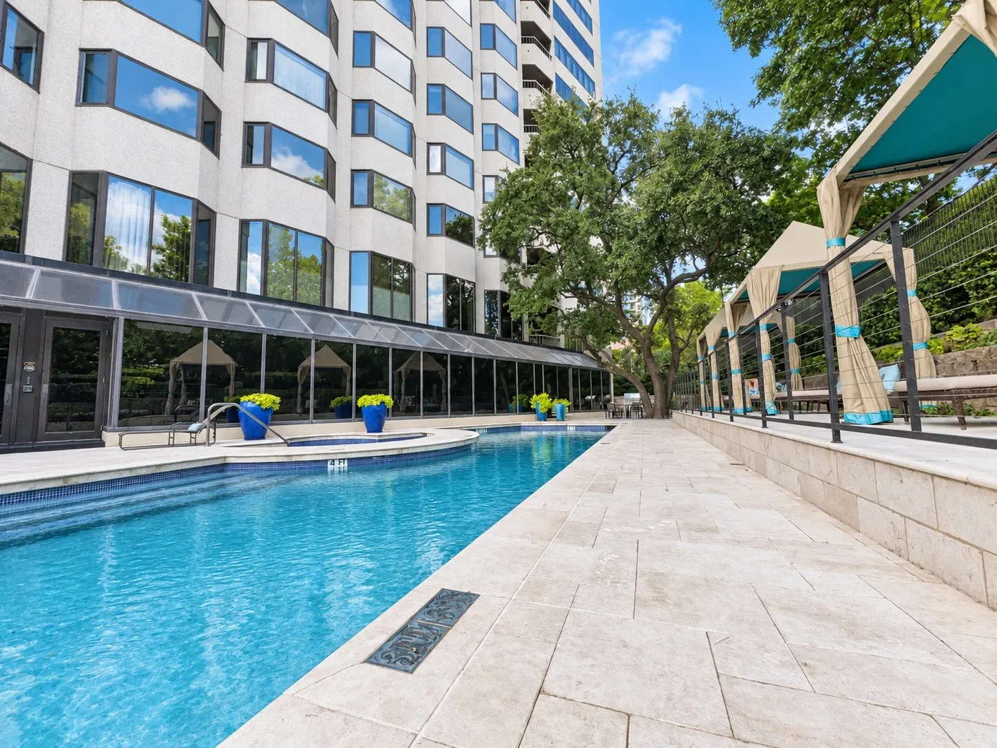 Outdoor swimming pool with integrated spa, bordered by a textured stone patio and covered seating areas