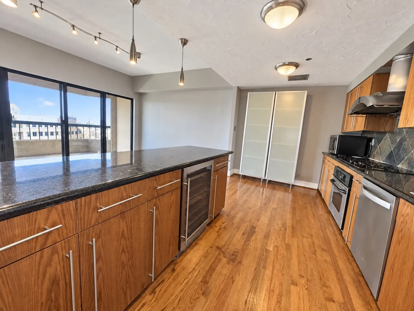 Kitchen featuring wood cabinetry, stainless steel appliances, dark stone countertops, wood-finish flooring, and a built-in beverage cooler