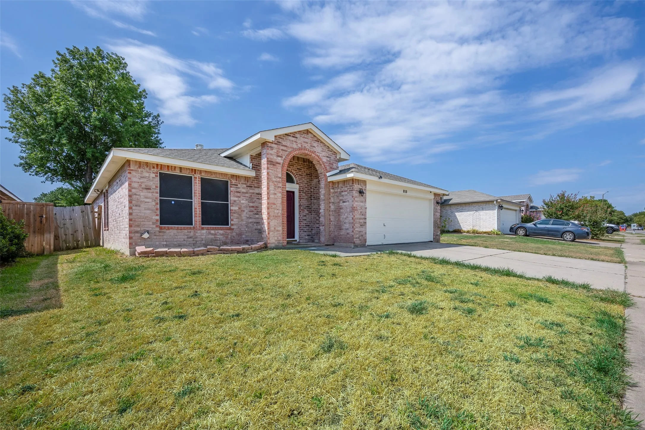 Brick exterior with an arched entryway, attached garage, concrete driveway, and a fenced side yard