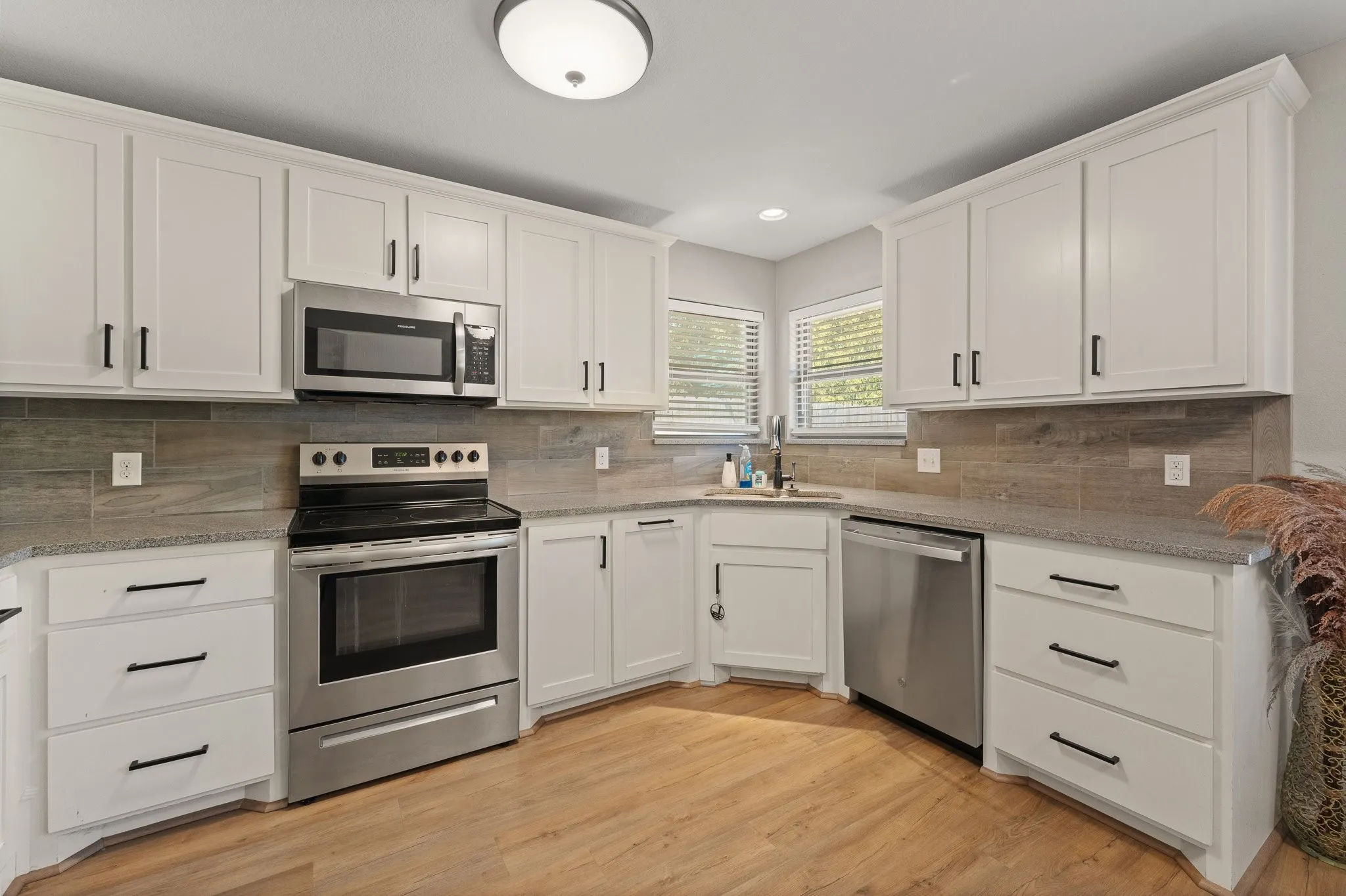 White shaker cabinetry with black hardware, wood-finish flooring, stainless steel appliances, and a tiled backsplash