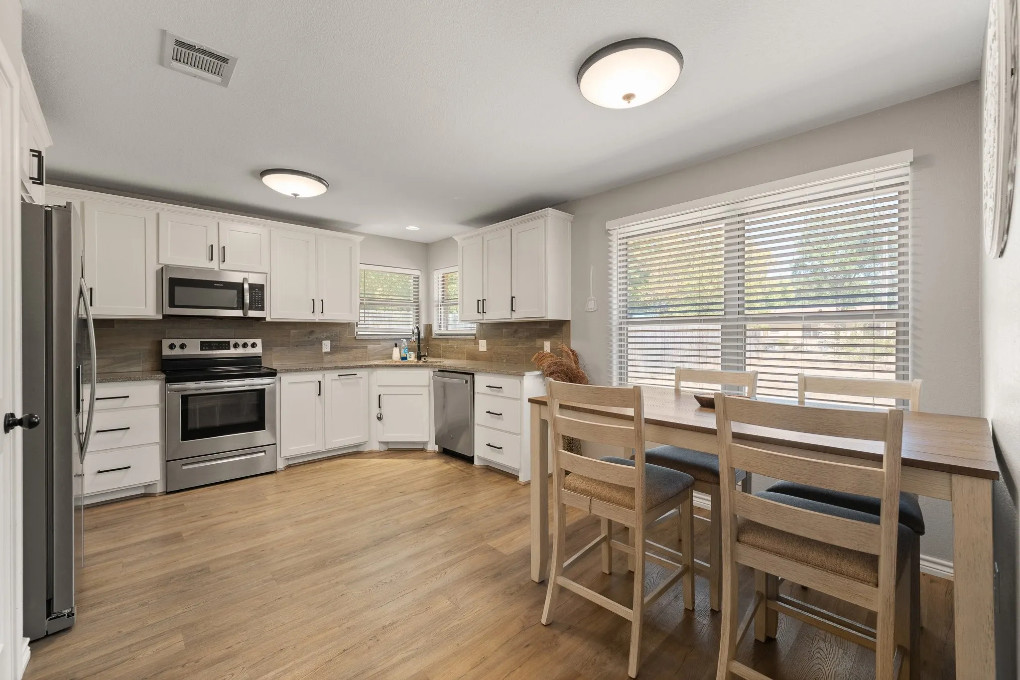 Kitchen featuring white cabinetry, stainless steel appliances, wood-finish flooring, and a tiled backsplash