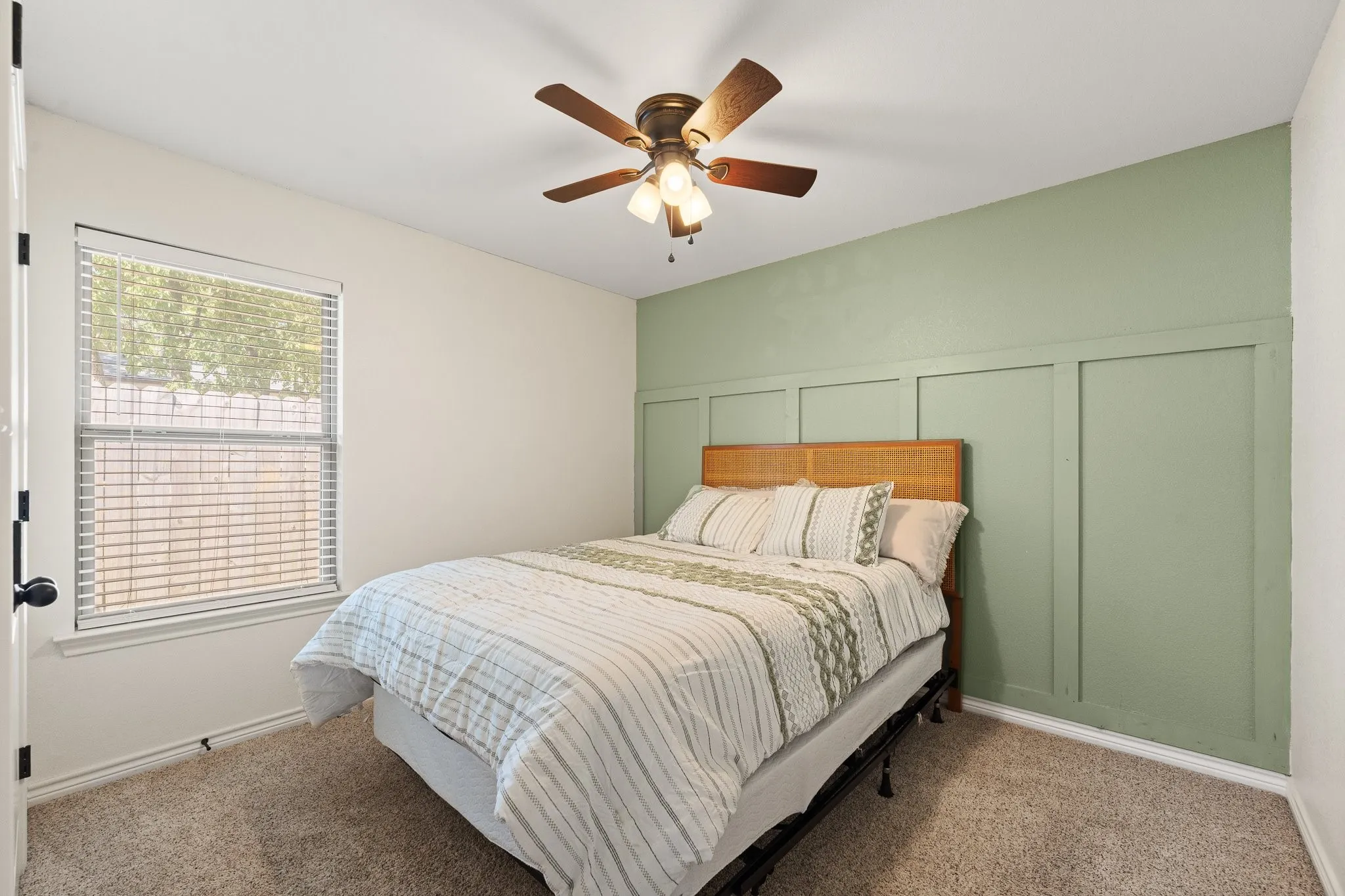 Carpeted flooring, a window with blinds, a ceiling fan with integrated lighting, and an accent wall with wainscoting