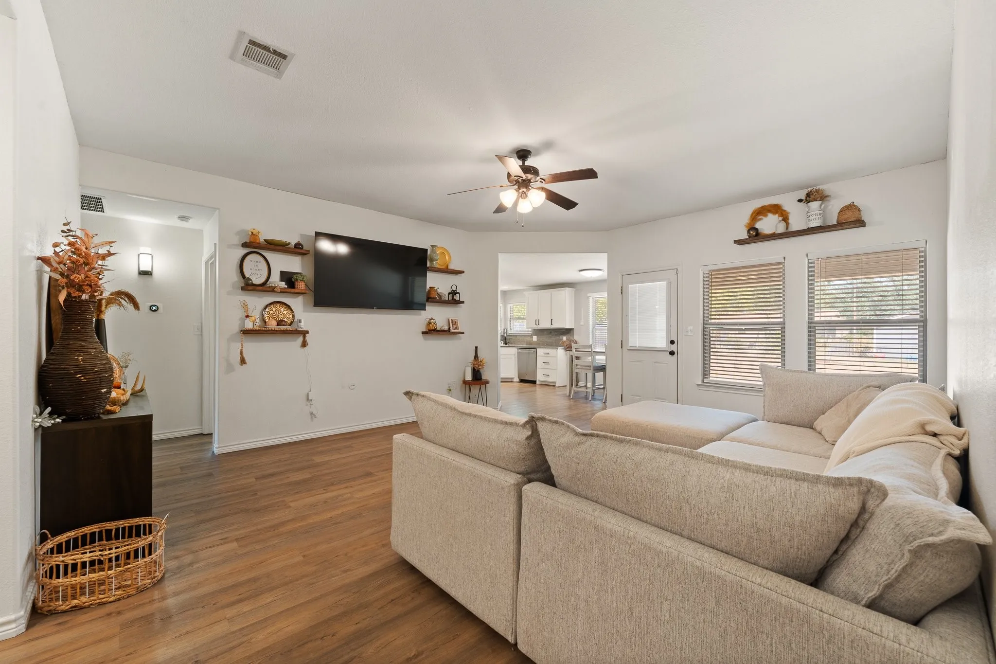 Spacious living area featuring wood-finish flooring, a ceiling fan, and multiple windows with blinds