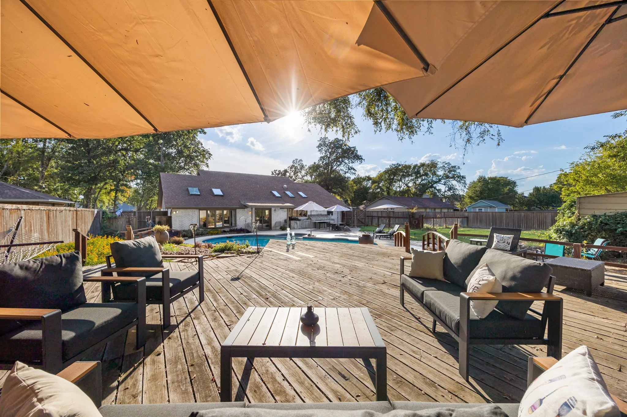 Expansive wood-finish deck with multiple seating areas, a built-in swimming pool, and a white stucco exterior with multiple skylights