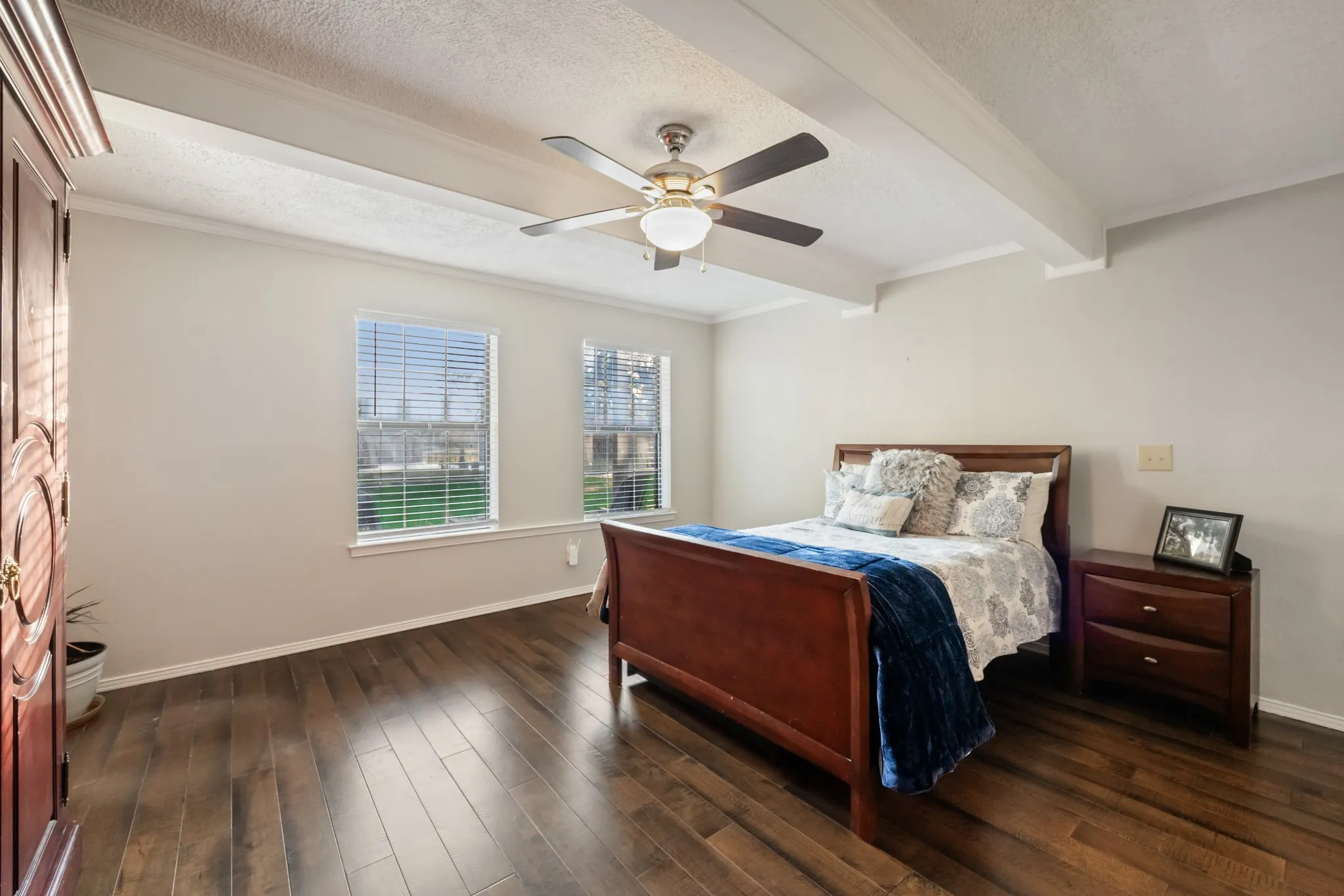 Wood-finish flooring with dual windows, a ceiling fan with integrated lighting, and exposed ceiling beams