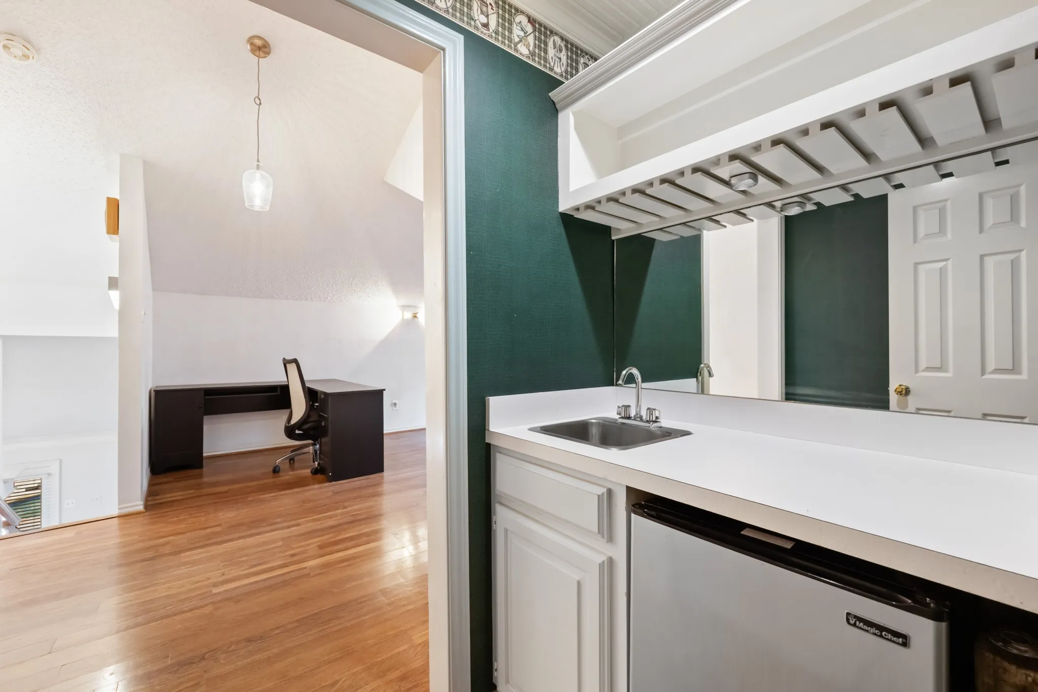 Wet bar featuring a stainless steel sink, white countertop, white cabinetry, and an integrated wine glass rack