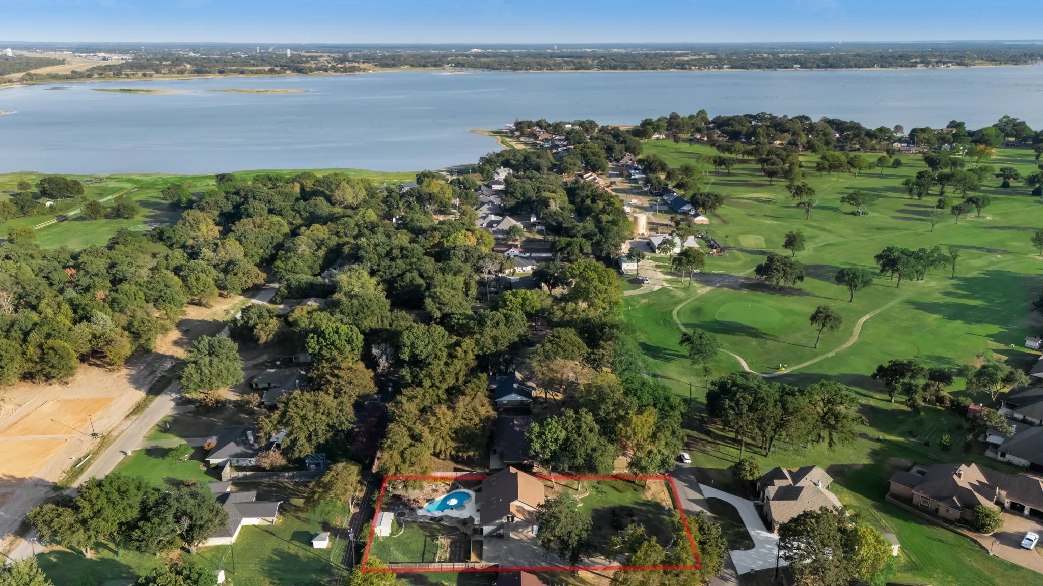 Expansive property featuring a private swimming pool, mature trees, and a manicured lawn, with a prominent lake backdrop and golf course proximity