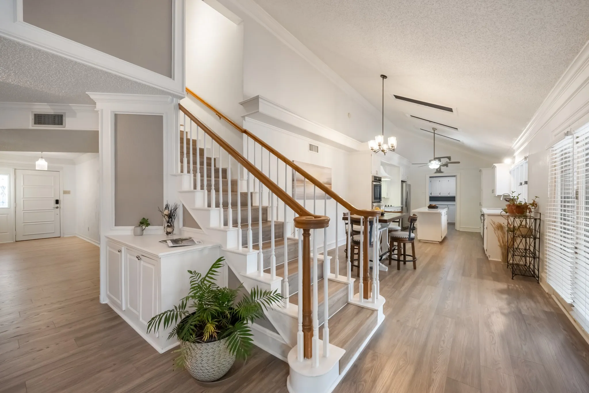 Wood-finish flooring throughout, a staircase with wood handrails, a built-in cabinet with a countertop, an entry door with sidelight, and a vaulted ceiling with exposed beams