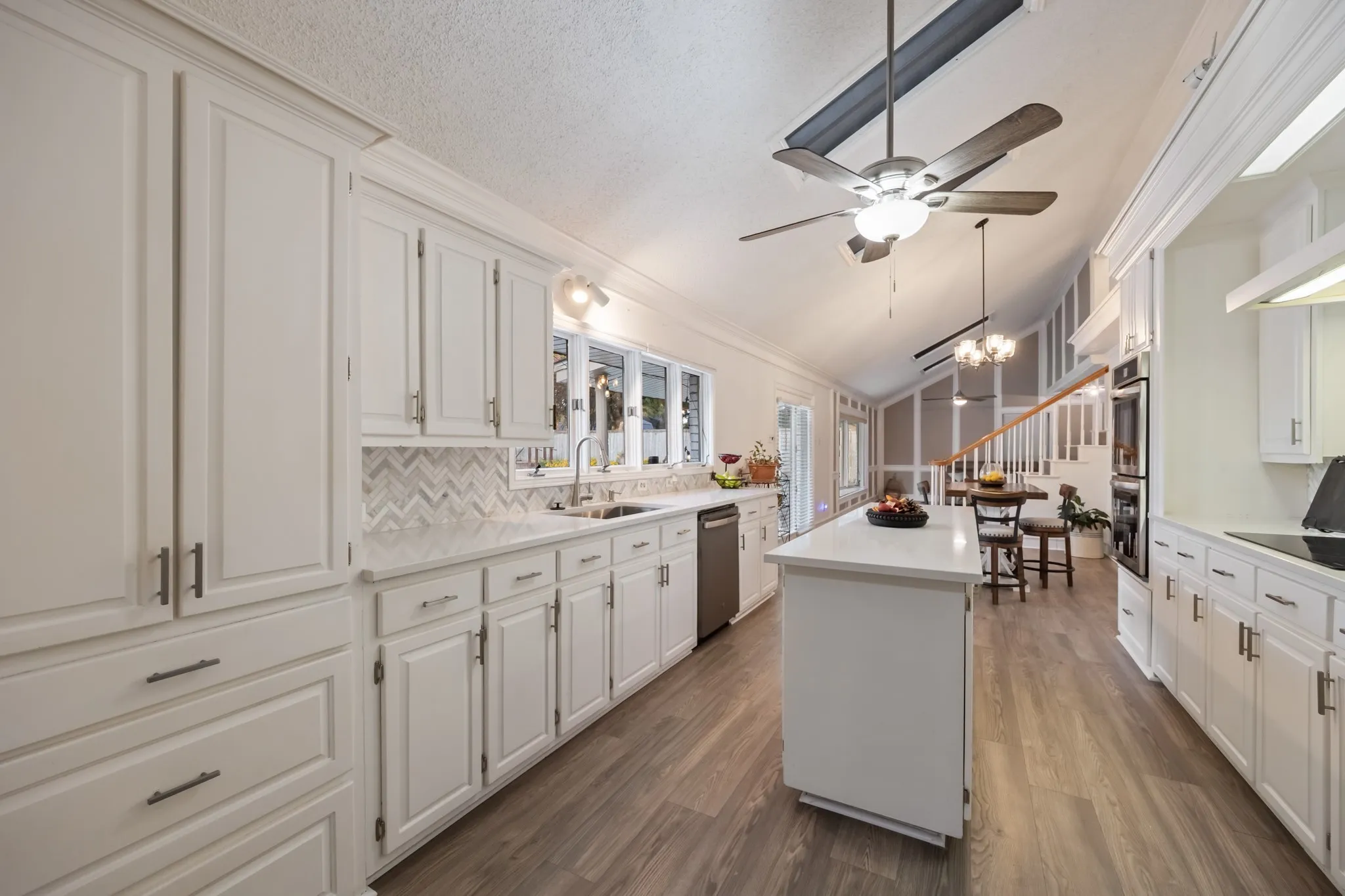 Kitchen featuring white cabinetry, chevron pattern tile backsplash, center island with solid surface countertop, wood-finish flooring, and vaulted ceiling