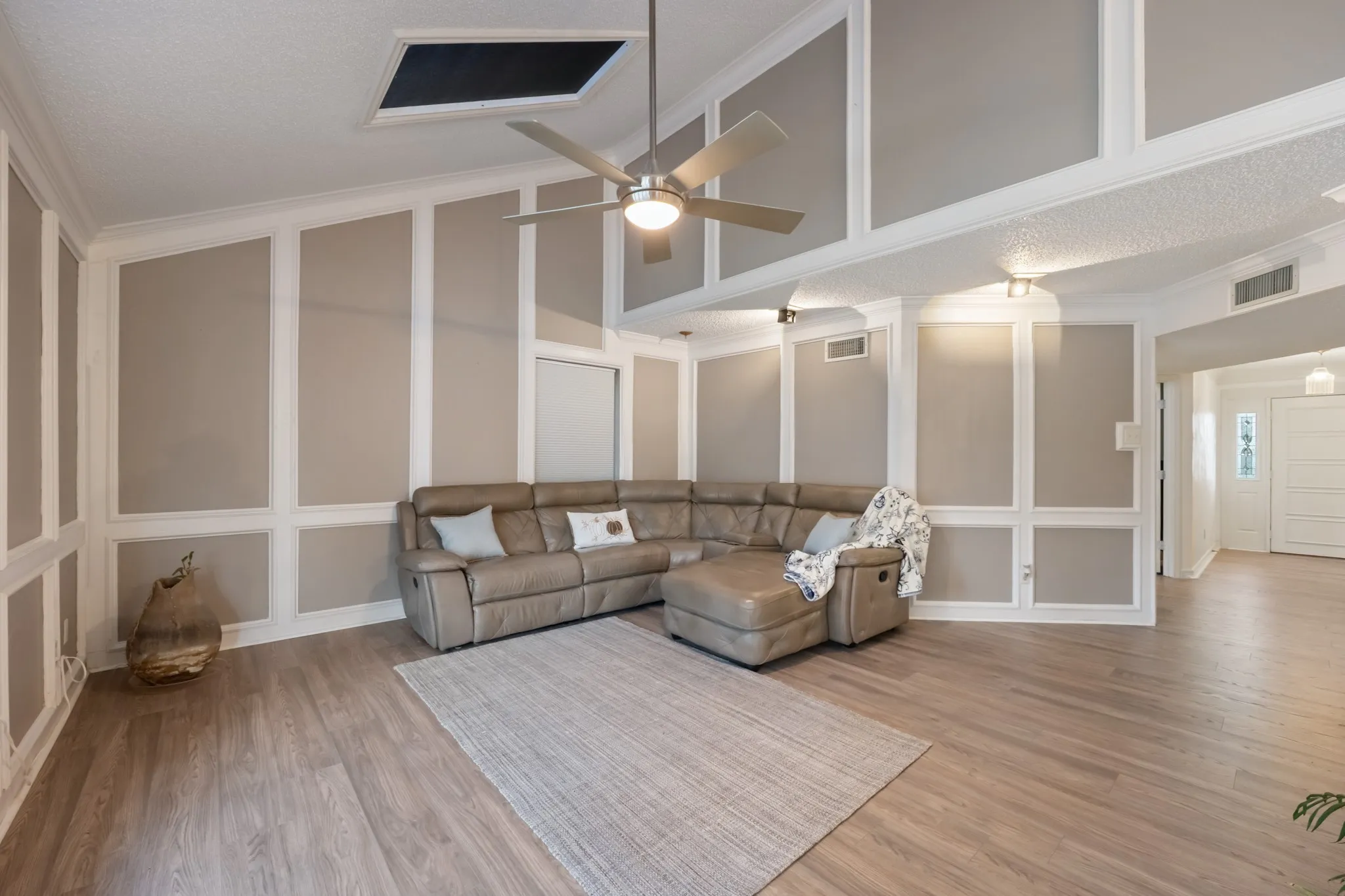Vaulted ceiling with skylight, wood-finish flooring, accent wall paneling, and ceiling fan