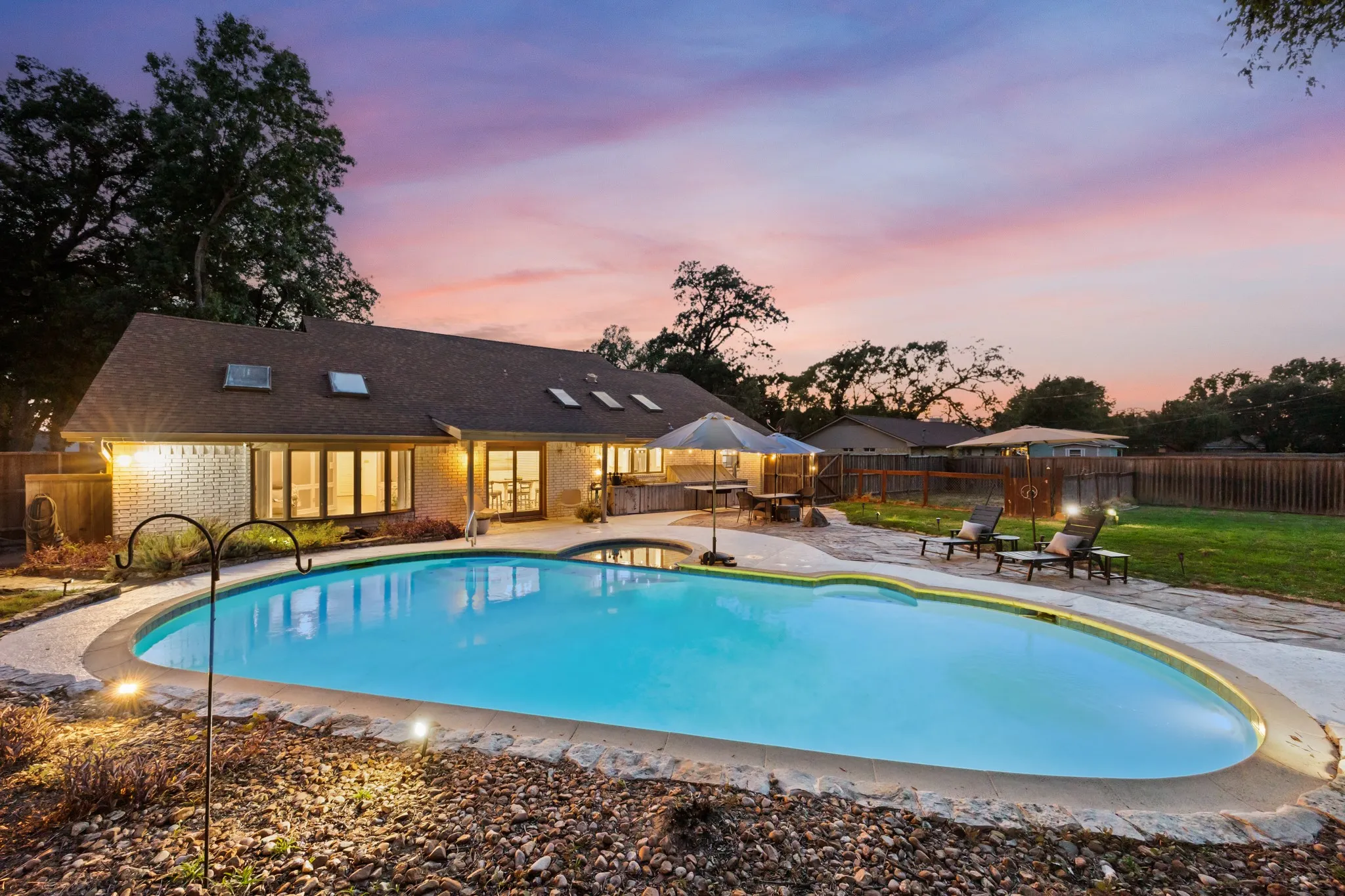 Expansive backyard featuring a custom-shaped swimming pool, stone patio, and a manicured lawn