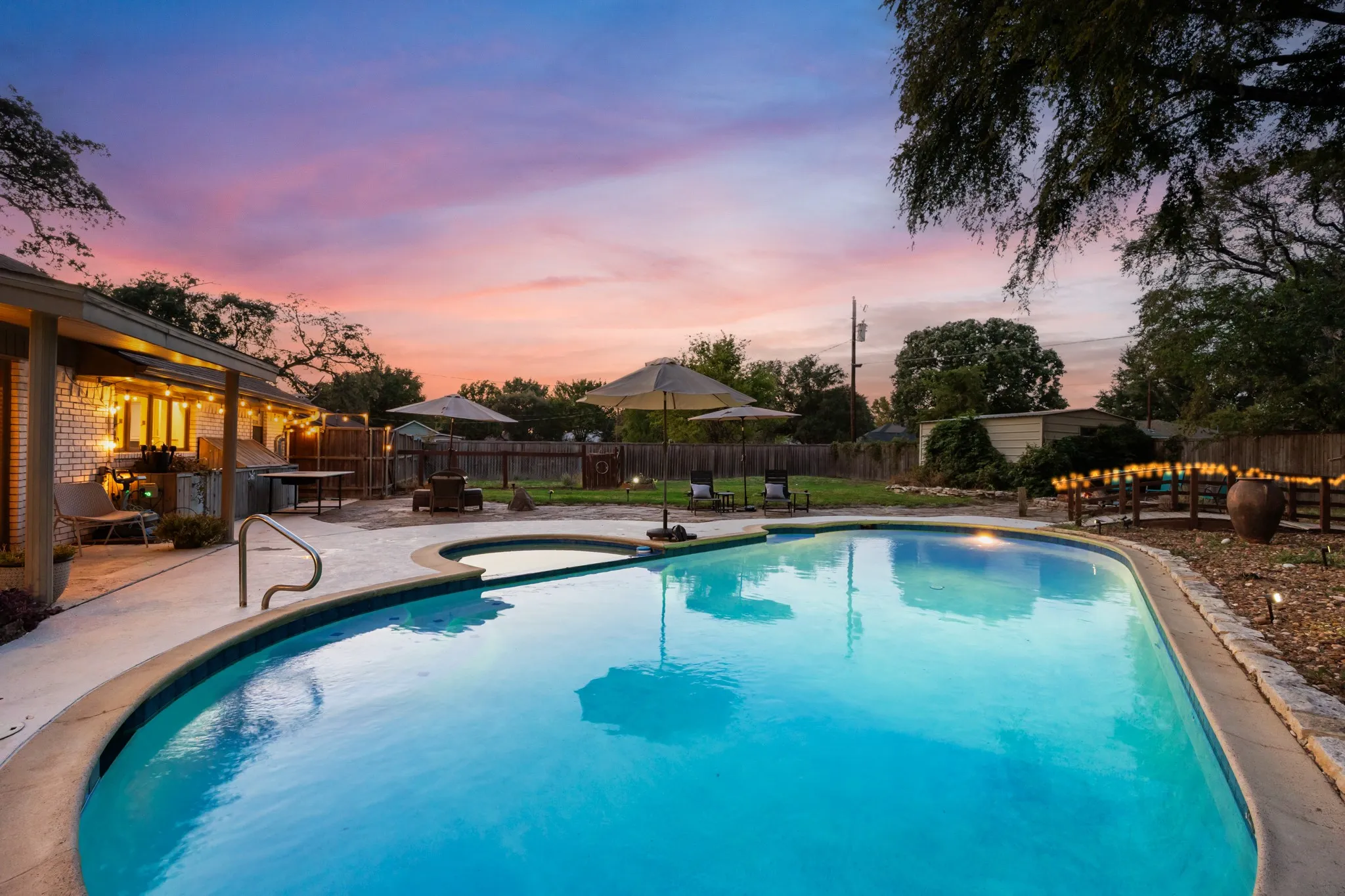 Expansive backyard featuring a built-in swimming pool and integrated spa, complemented by a covered patio, paved decking, and perimeter fencing
