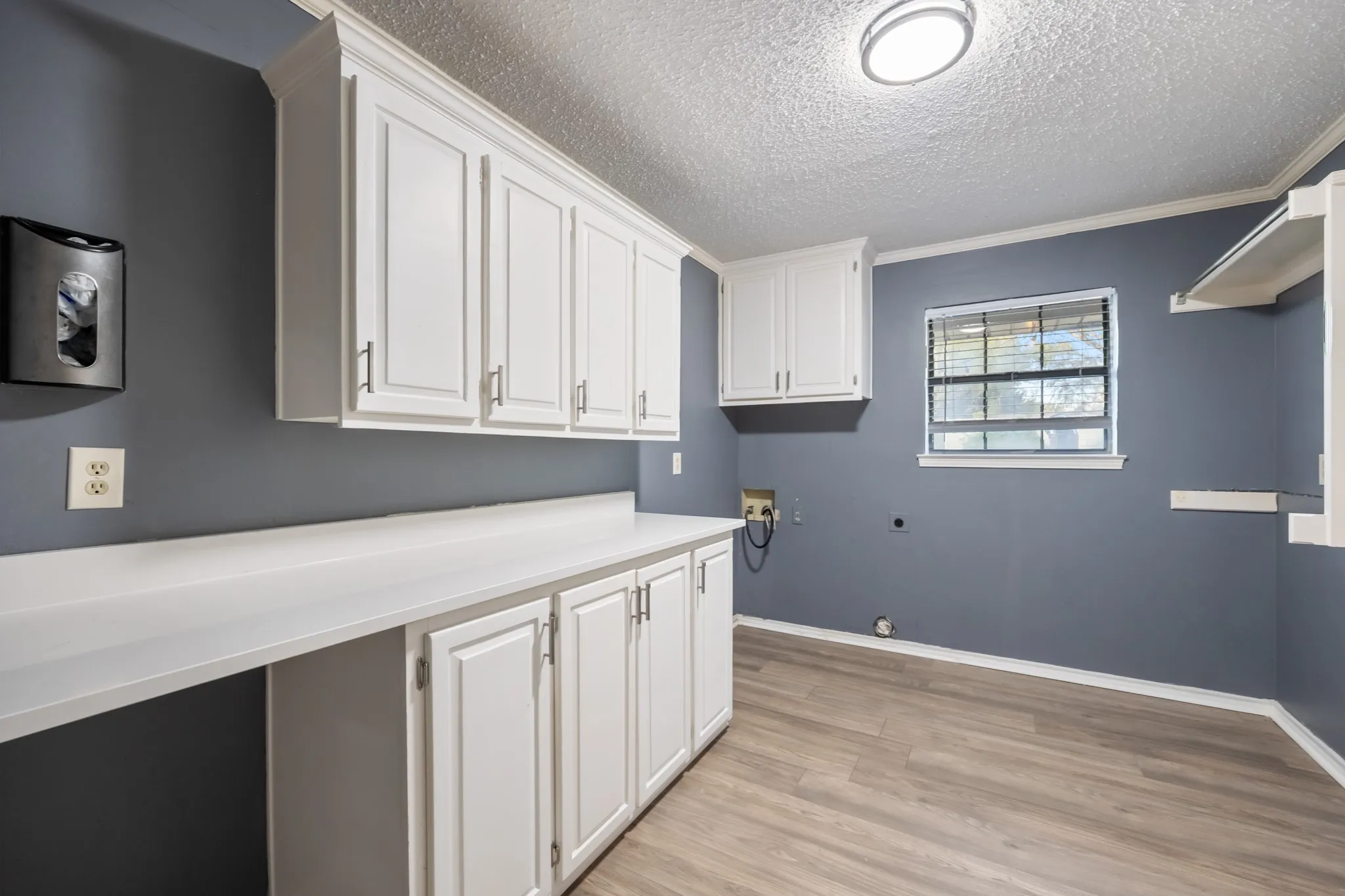 White cabinetry, extensive counter space, wood-finish flooring, ceiling-mounted lighting, and a window with blinds