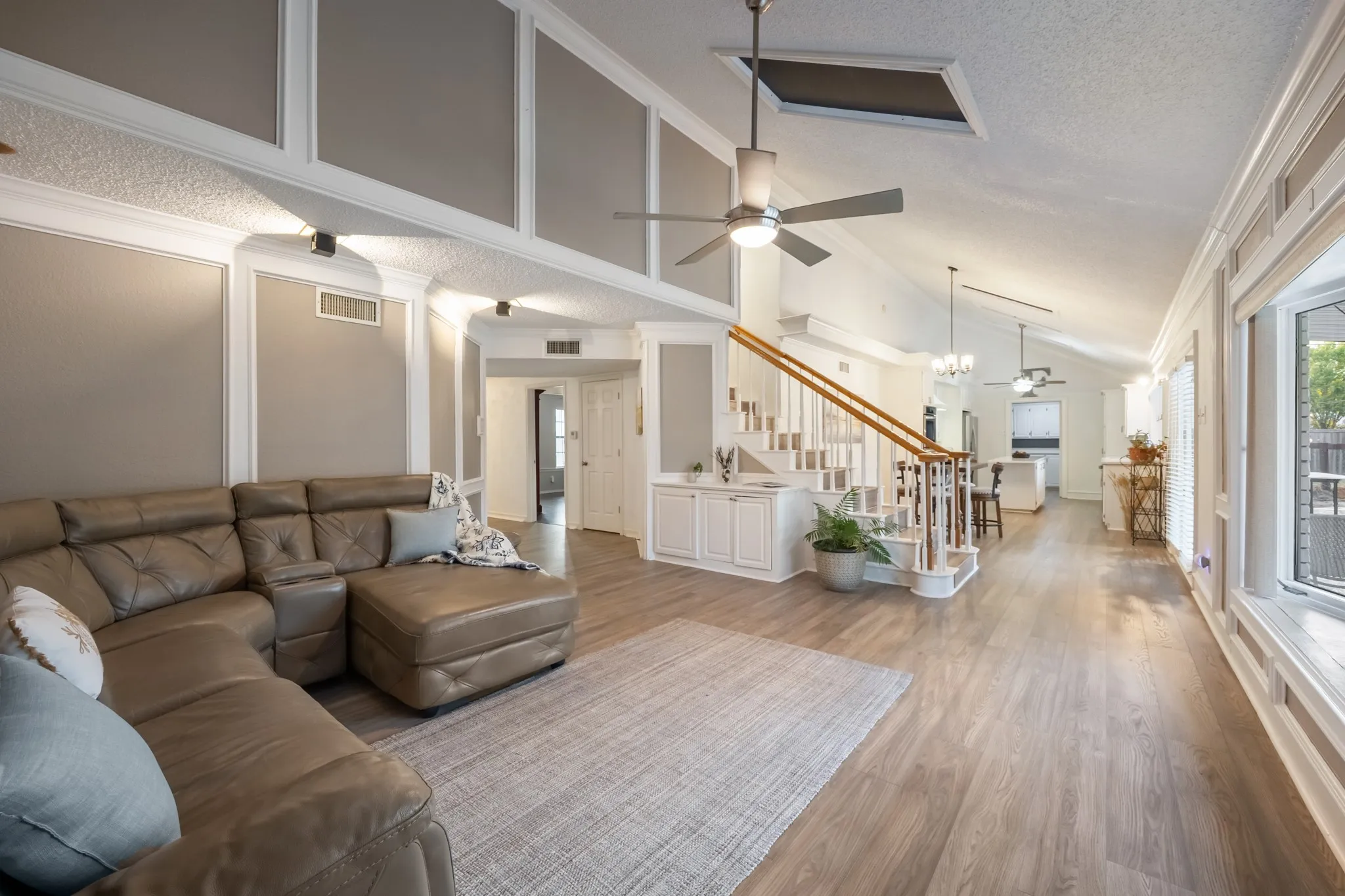 Vaulted ceilings with skylight, wood-finish flooring, built-in cabinetry, staircase with wood handrail, and multiple ceiling fans