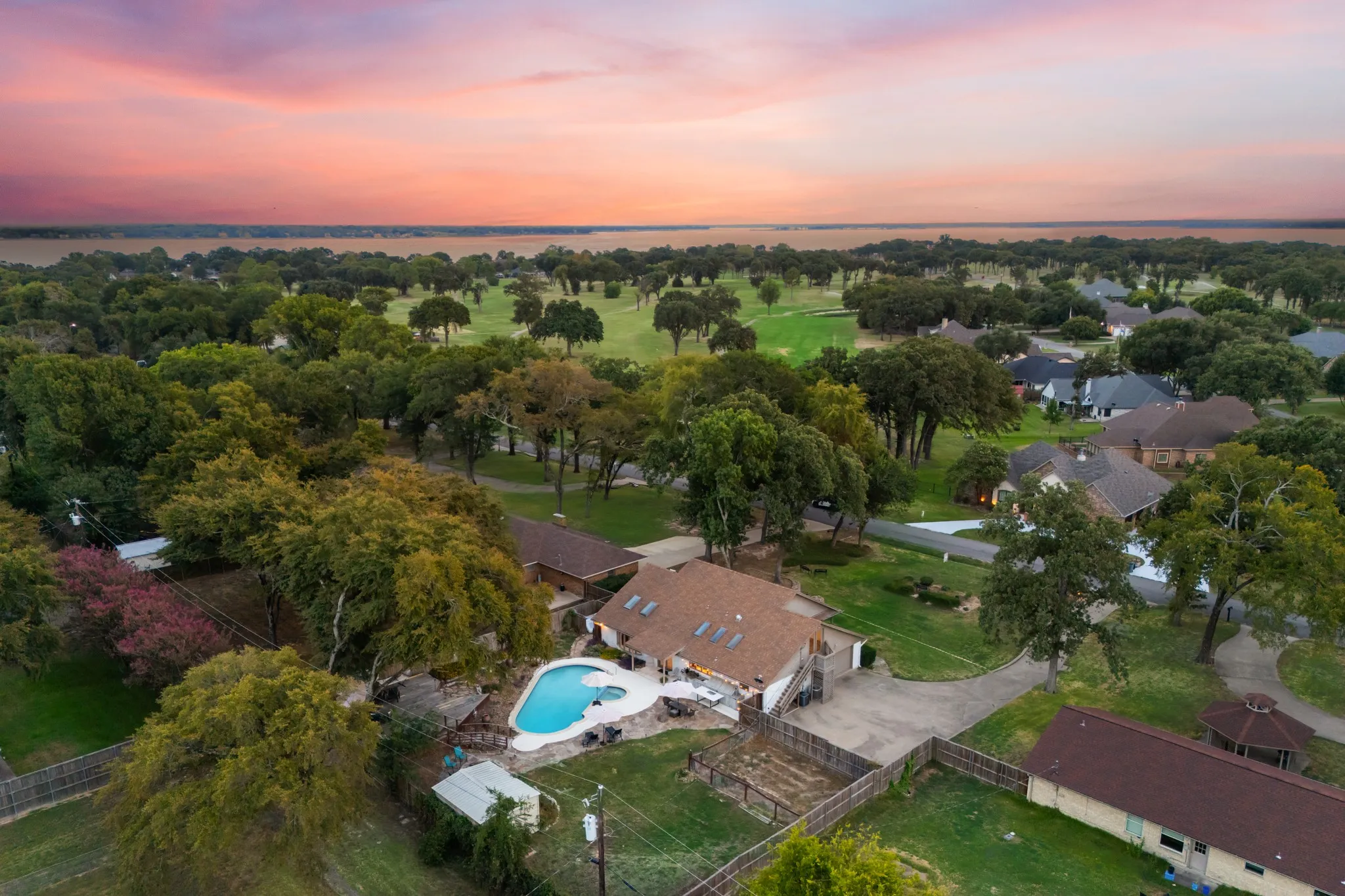 Aerial perspective featuring a residential property with a swimming pool, adjacent to a golf course and a body of water