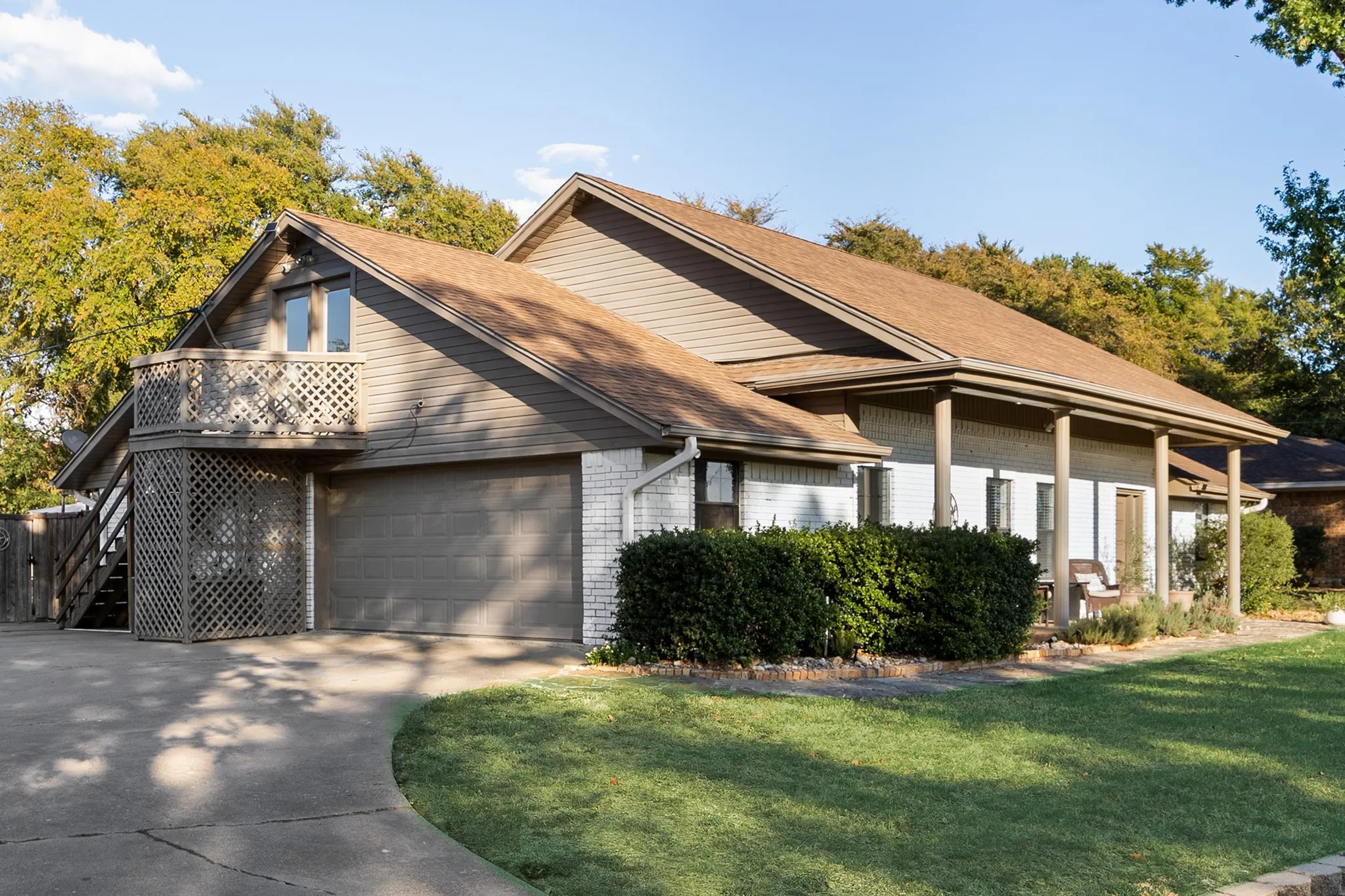Attached two-car garage with a private balcony, covered porch with support columns, white brick exterior, and a manicured lawn