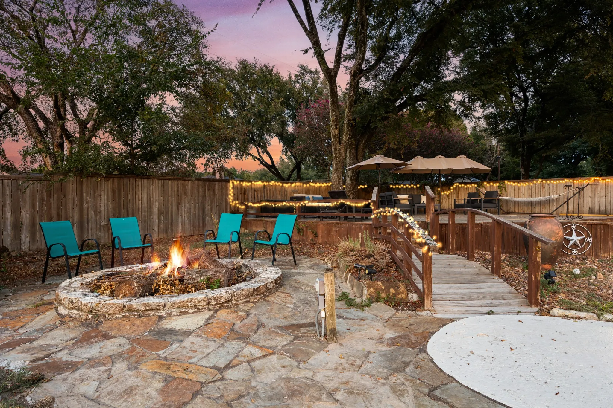 Expansive outdoor living area featuring a stone fire pit, flagstone patio, raised wooden deck, and wooden bridge