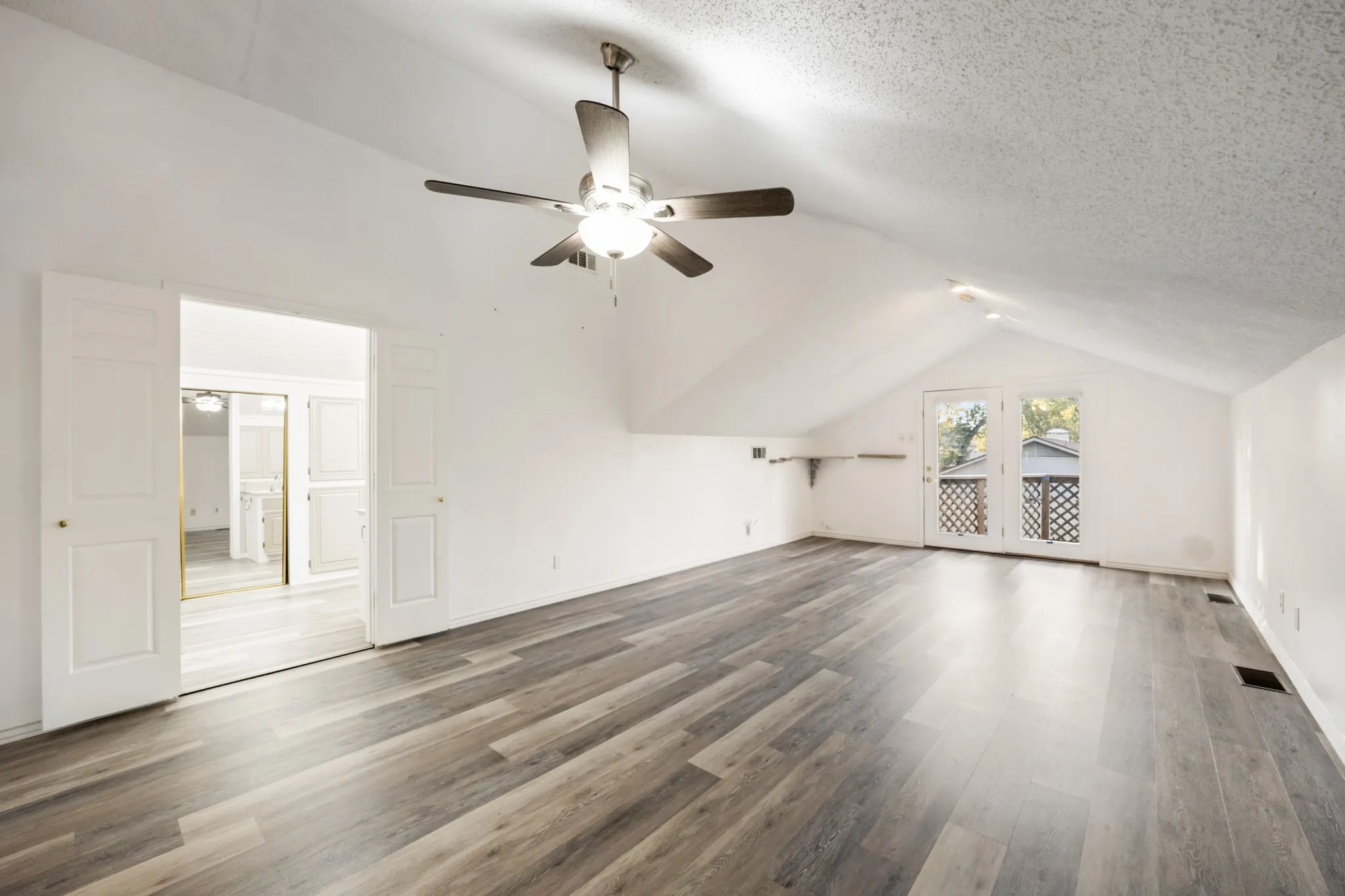 Upstairs 2nd master or guest room with private entrance. Vaulted ceiling with a ceiling fan, wood-finish flooring, white walls, double French doors, and double sliding doors