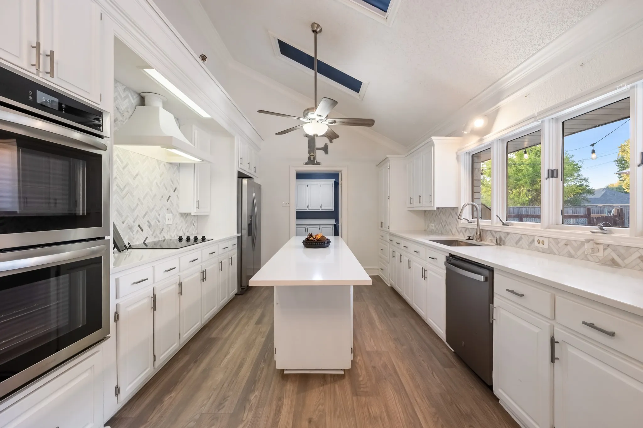White cabinetry, wood-finish flooring, white countertops, herringbone tile backsplash, and stainless steel appliances
