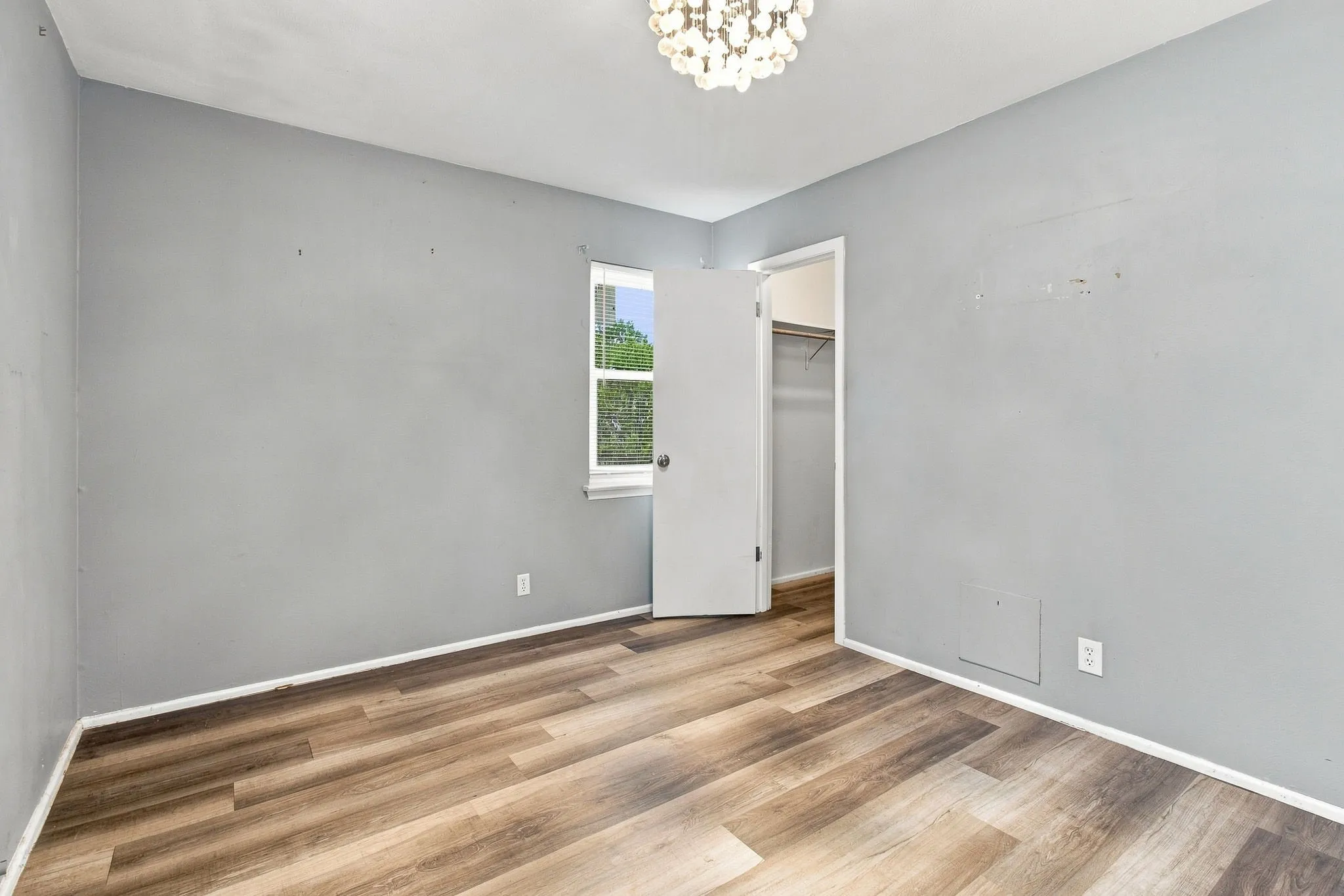 Wood-finish flooring, overhead chandelier lighting, and a window providing natural light