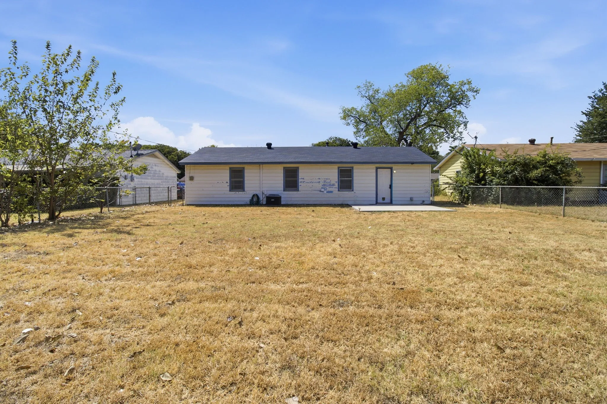Rear exterior with a concrete patio, white siding, and a dark shingle roof
