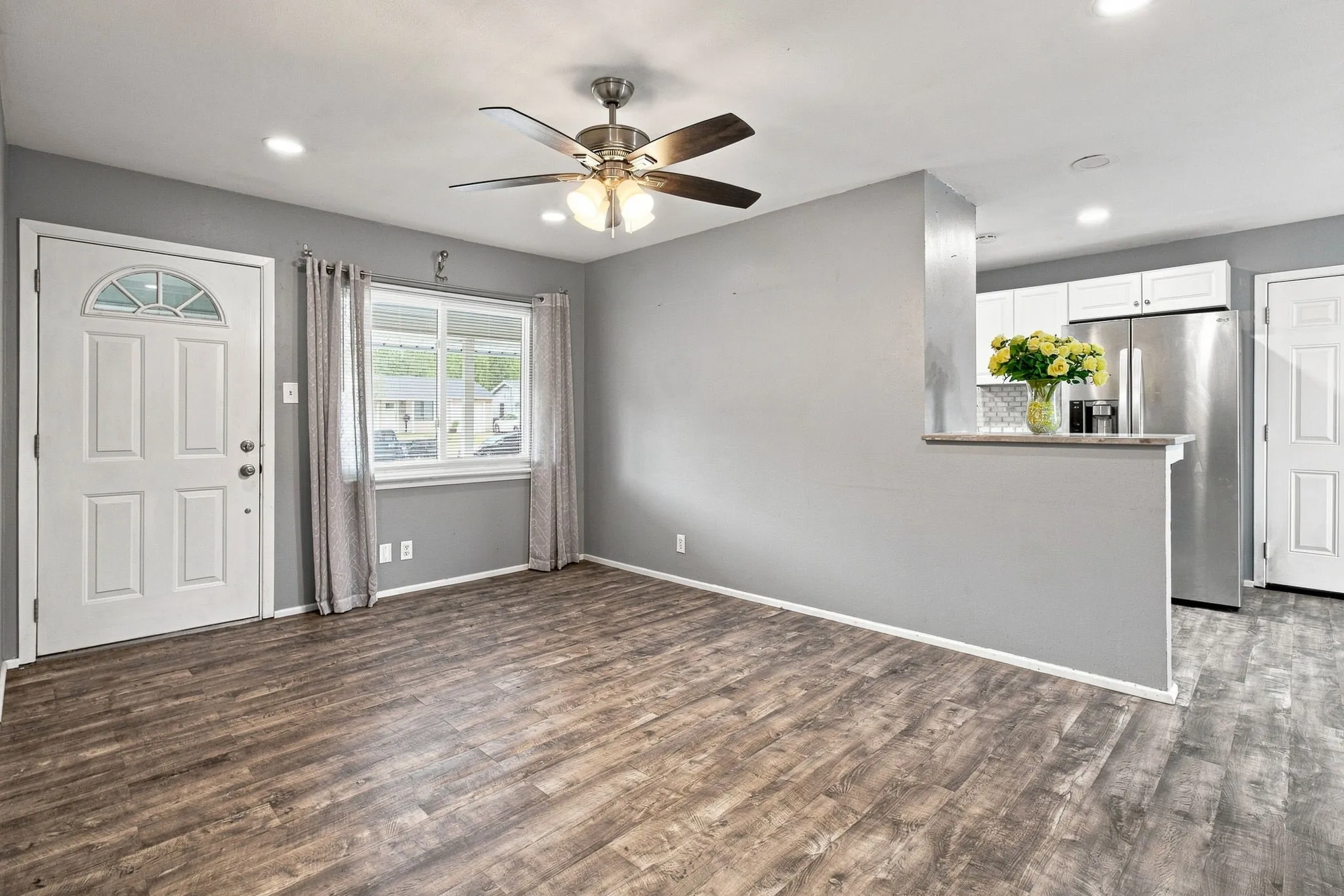 Wood-finish flooring, recessed lighting, ceiling fan, white paneled door with glass insert, and a kitchen pass-through with a countertop