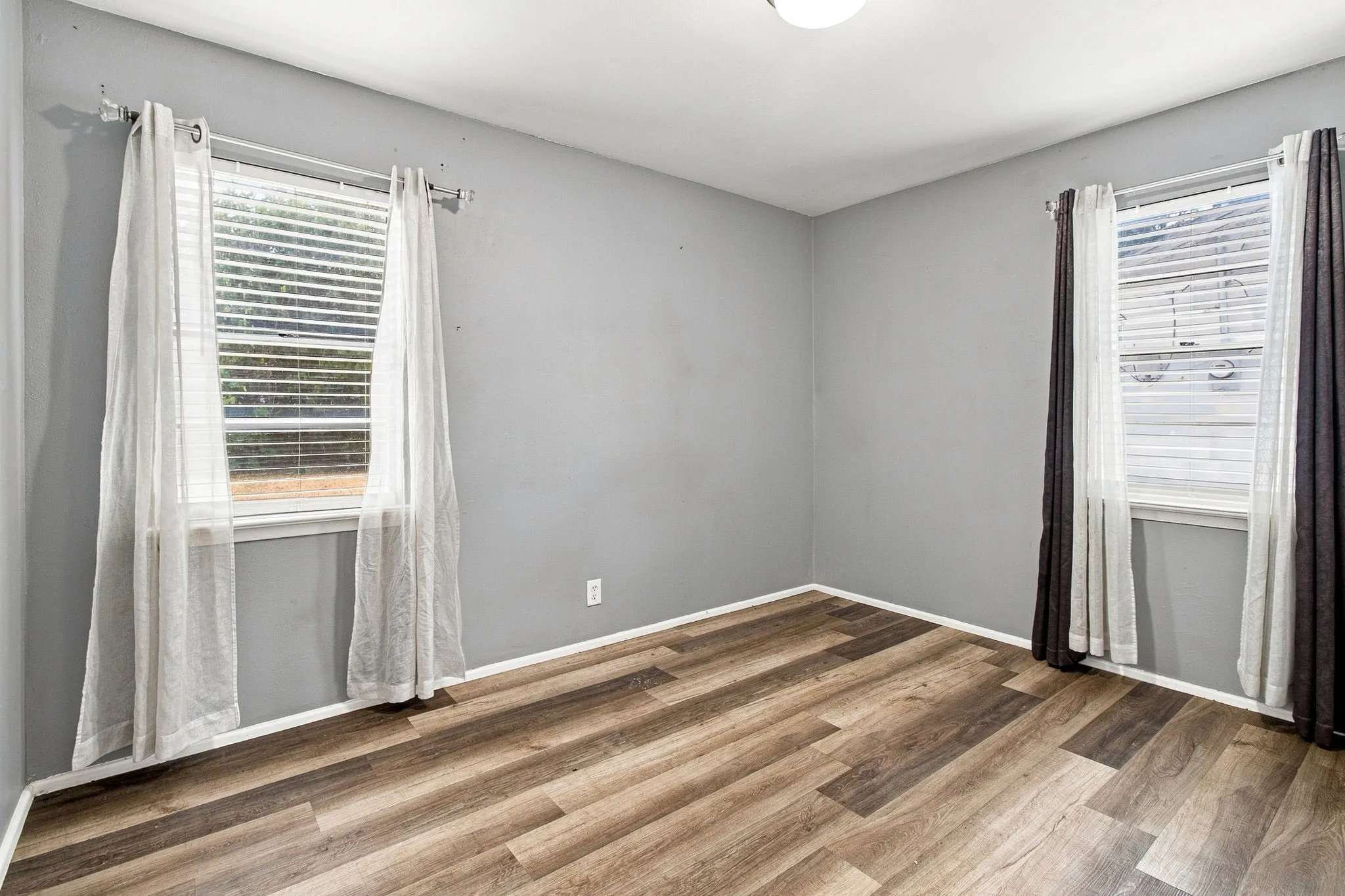 Wood-finish flooring with white trim, two windows, and a ceiling-mounted light fixture