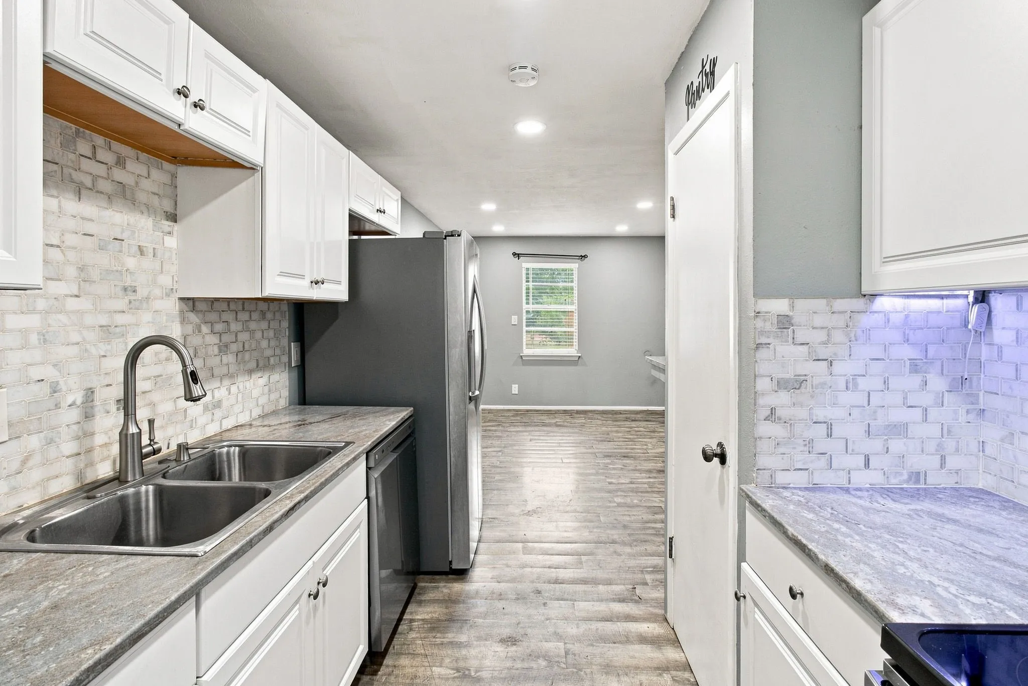 Kitchen featuring white cabinetry, dual basin stainless steel sink with gooseneck faucet, light-toned stone-look countertops, and brick-patterned tile backsplash