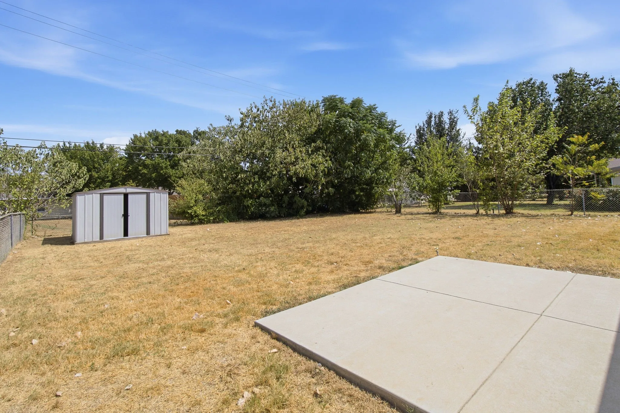 Expansive yard featuring a concrete patio, a metal storage shed, and mature perimeter trees