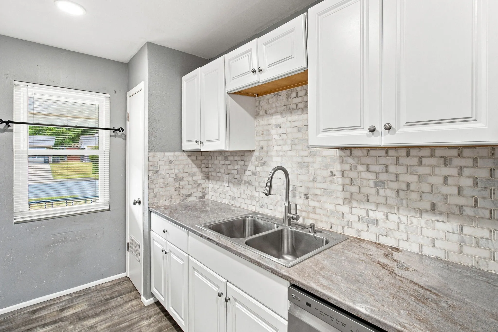 White cabinetry, dual basin stainless steel sink, brick-patterned backsplash, wood-finish flooring, and recessed lighting