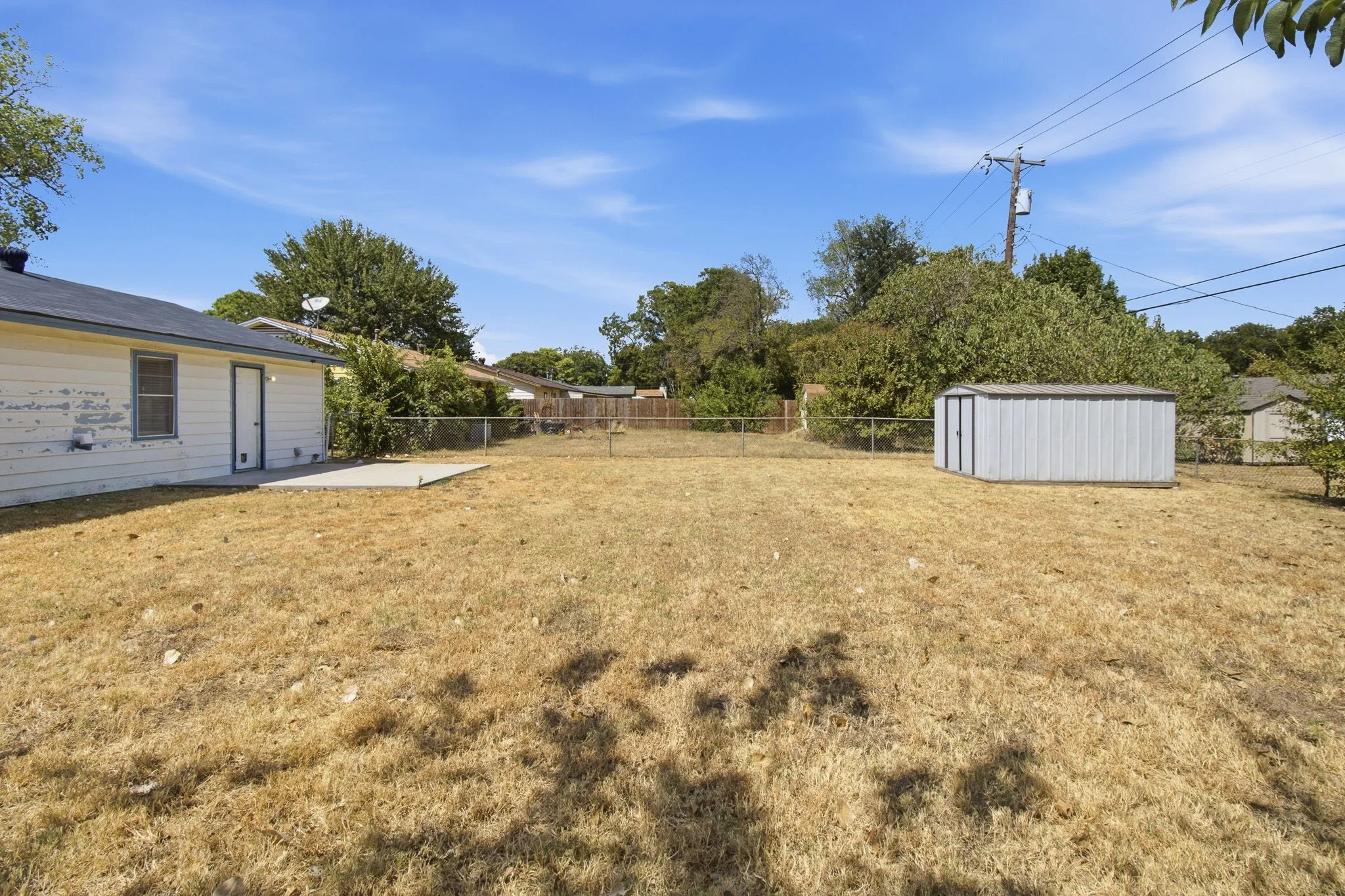 Expansive backyard featuring a chain-link fence, concrete patio, and a corrugated metal shed