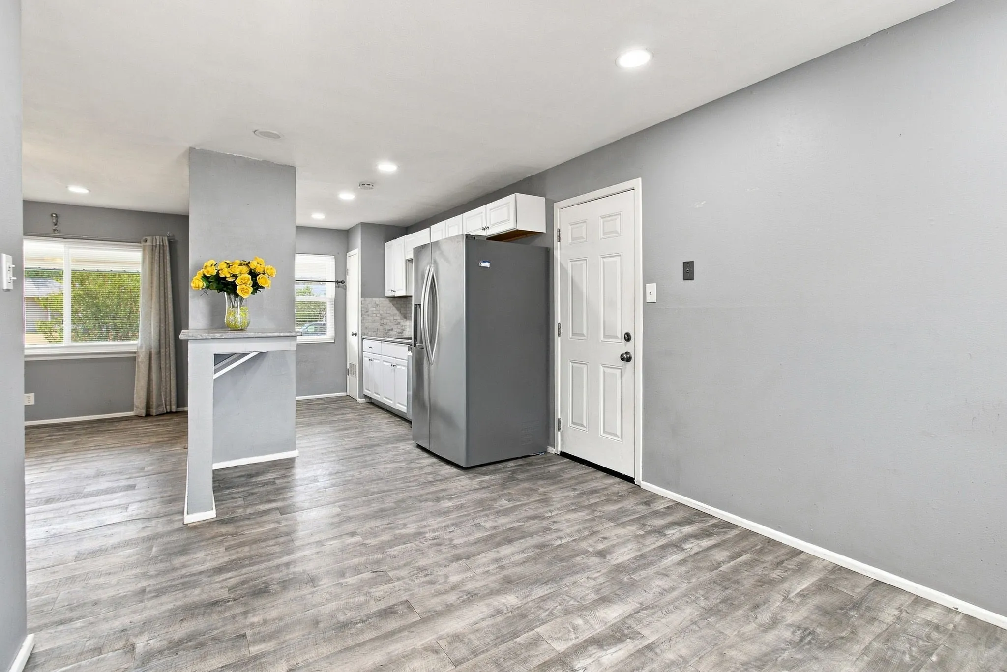 Wood-finish flooring, recessed lighting, white panel door, and a built-in kitchen pass-through with stone-finish top